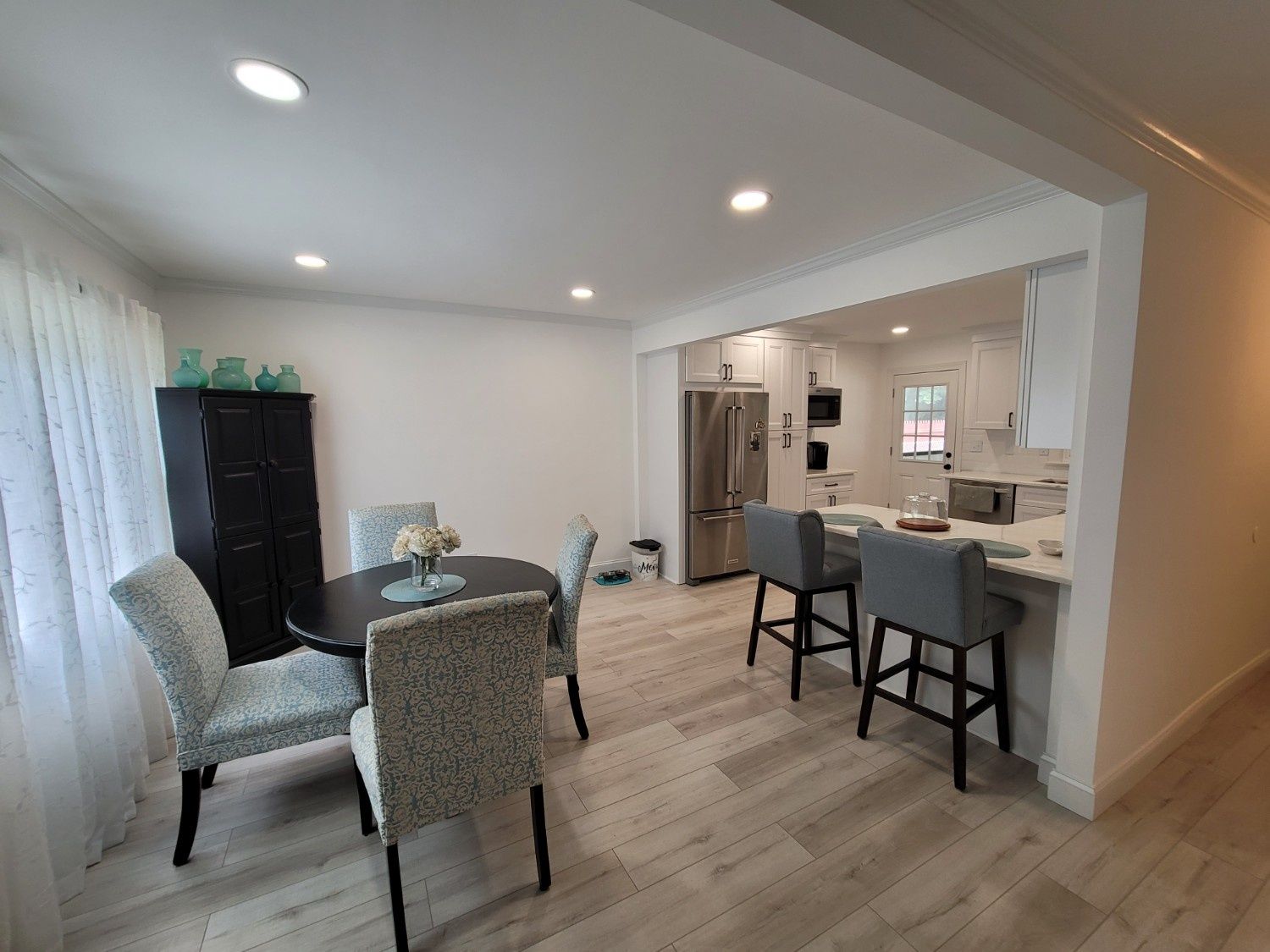 A bright dining and kitchen area with light wood-look floors, a small round table, and a kitchen island with bar stools.