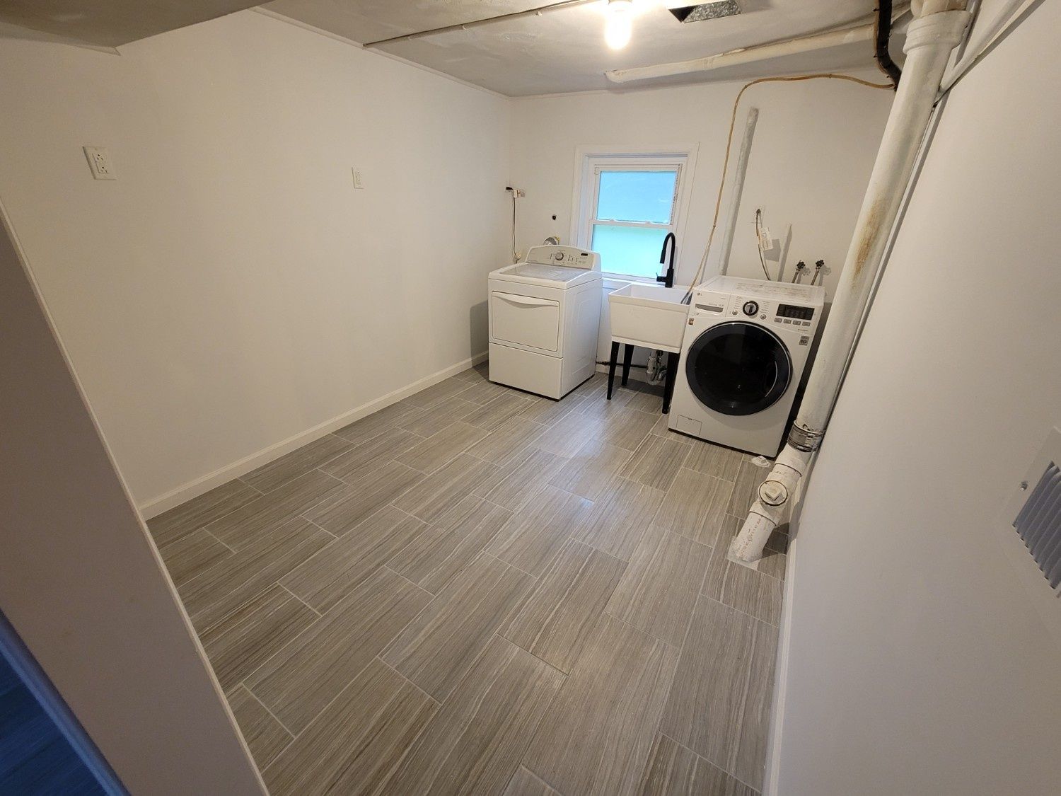 Laundry room with grey wood-look tile floors, a white washing machine, and a utility sink under a small window.
