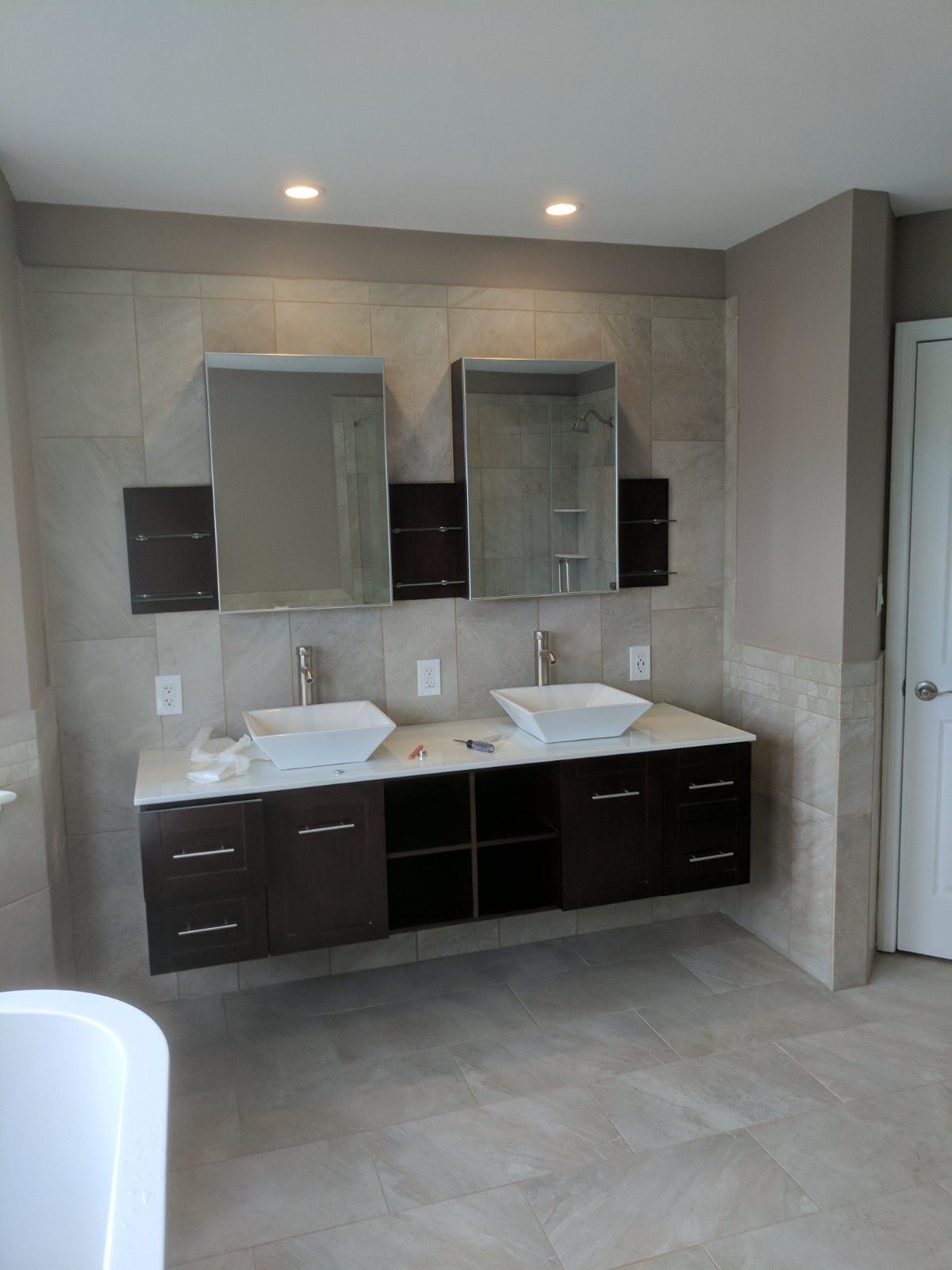 A floating dark wood double vanity with square vessel sinks, mirrors, and beige tile walls in a modern bathroom.
