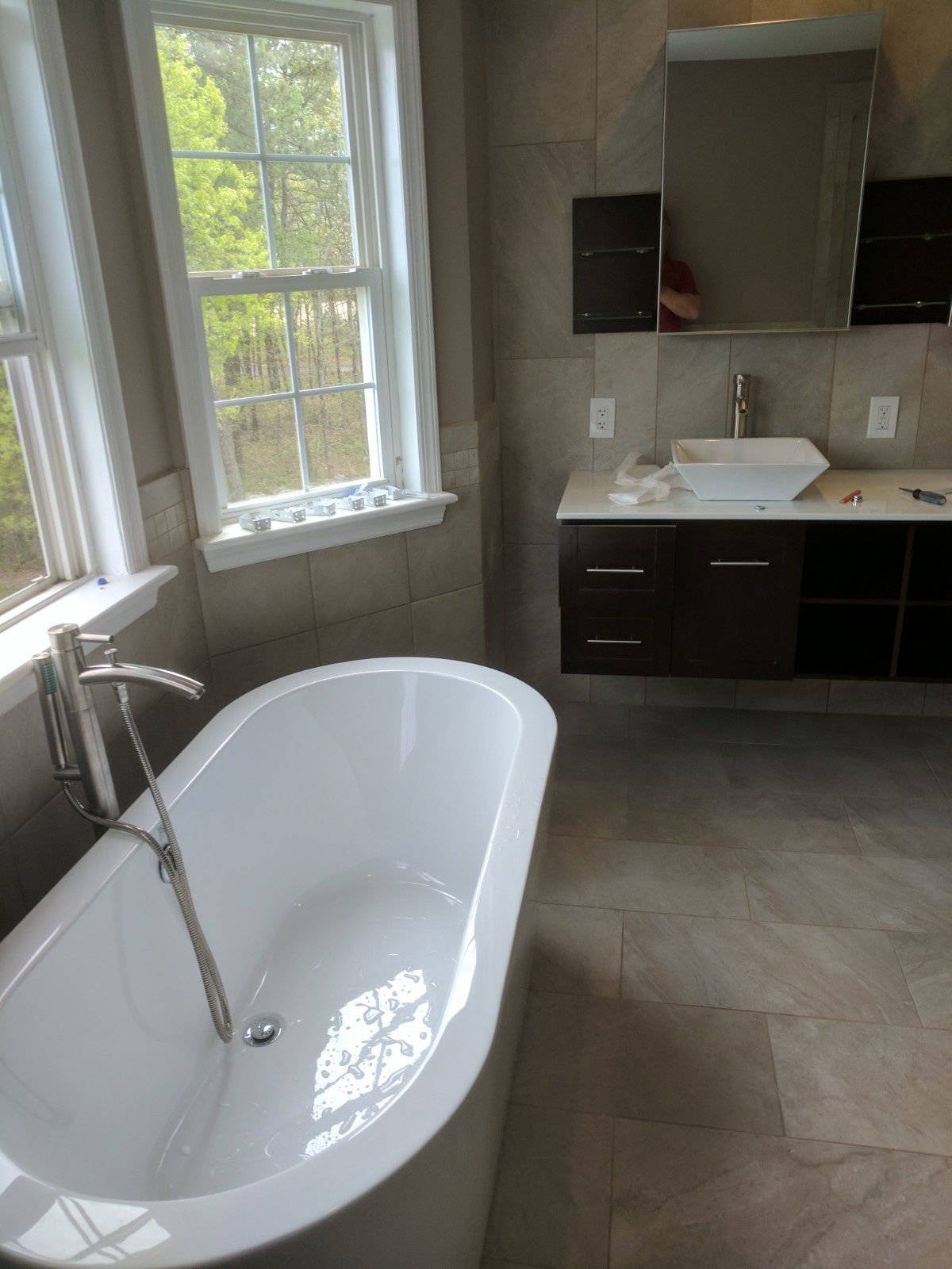 A modern bathroom featuring a white freestanding soaking tub, a dark wood vanity with a vessel sink, and large windows.