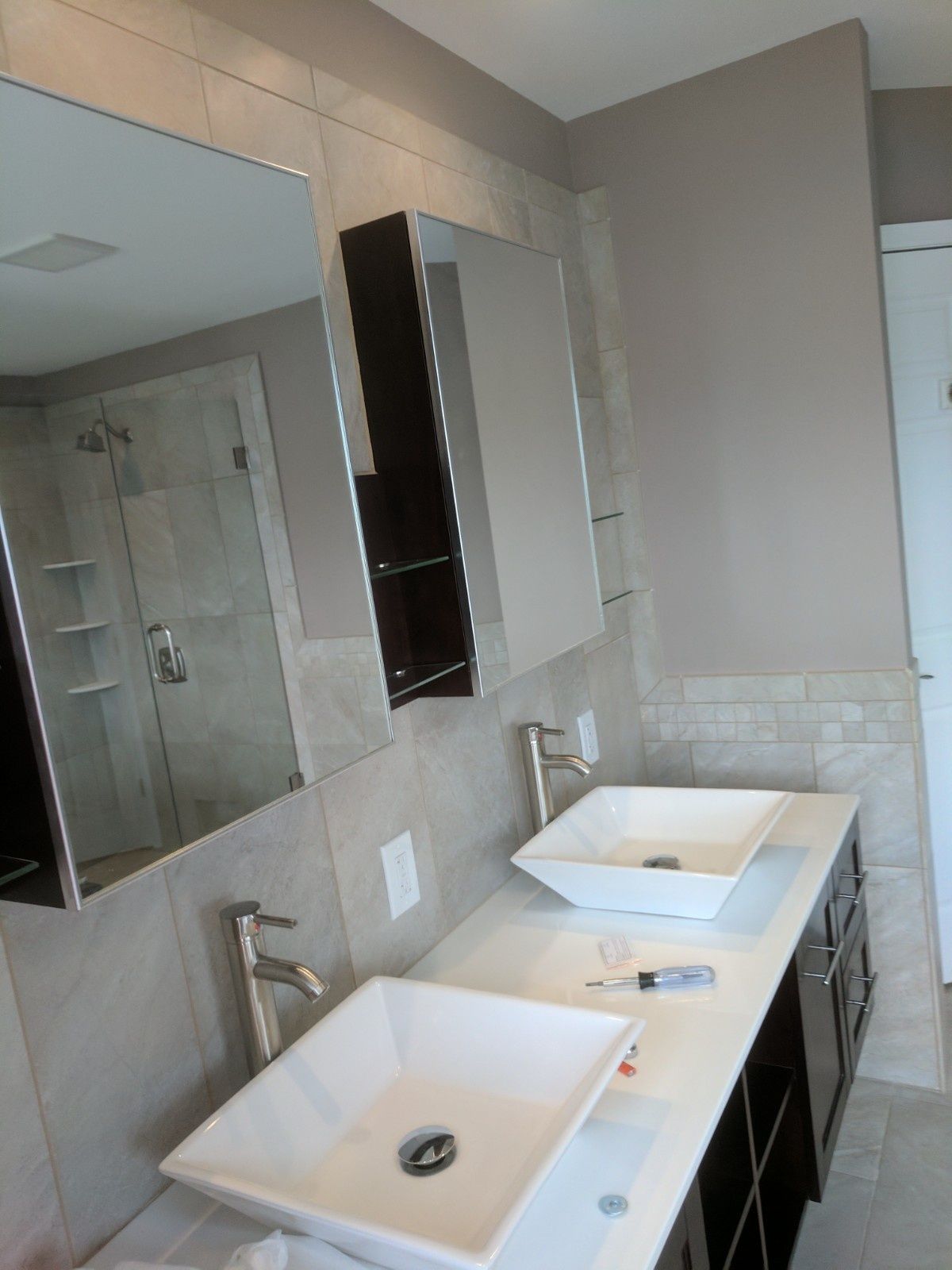 Modern bathroom vanity with dual white vessel sinks, silver faucets, and wall-mounted mirrors on tiled walls.