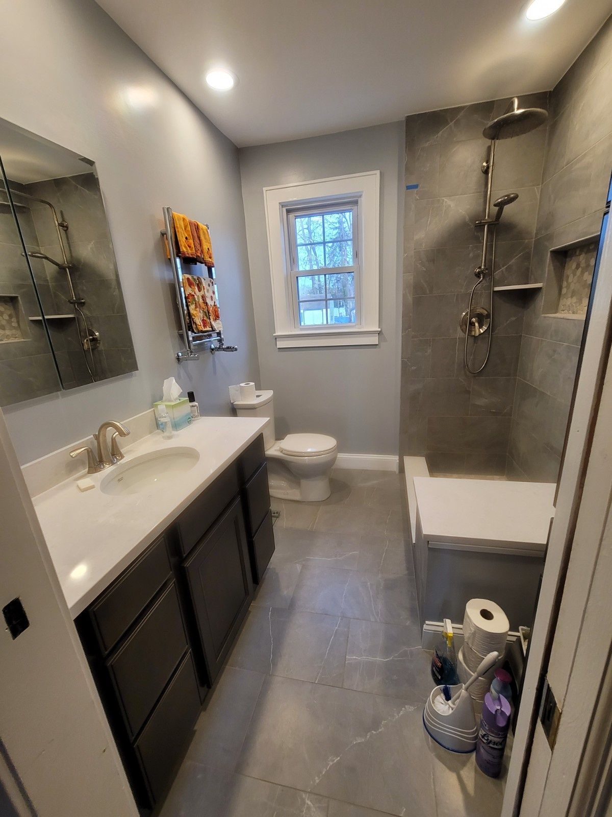 A small, modern bathroom with a dark gray vanity, white countertop, walk-in shower with gray tile, and a toilet.