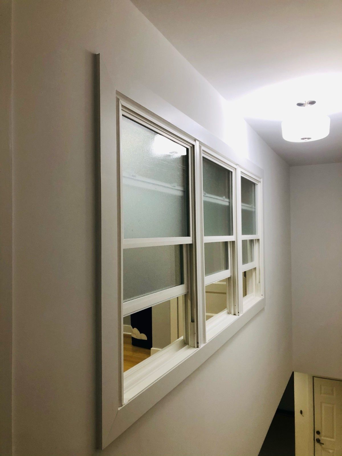A white-framed interior window with frosted glass panels set into a plain wall above a stairwell.