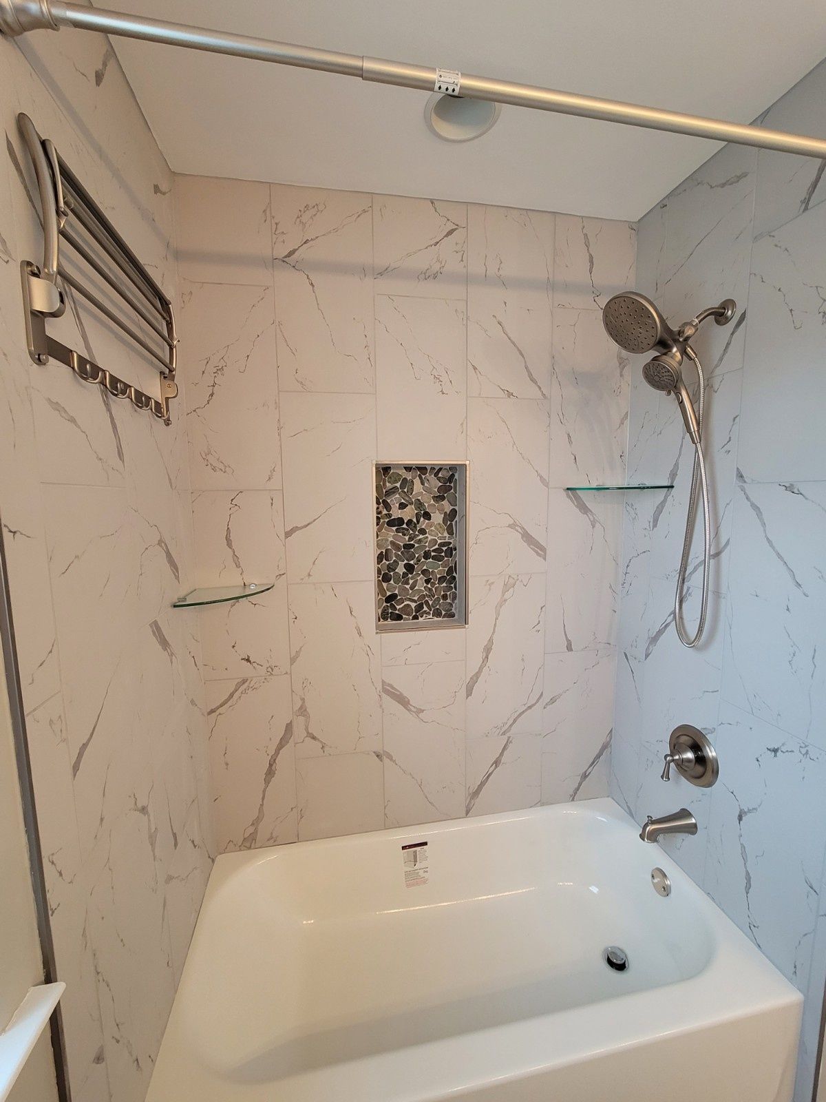 A shower-tub combo with white marble-patterned tile, a mosaic niche, chrome fixtures, and a glass corner shelf.
