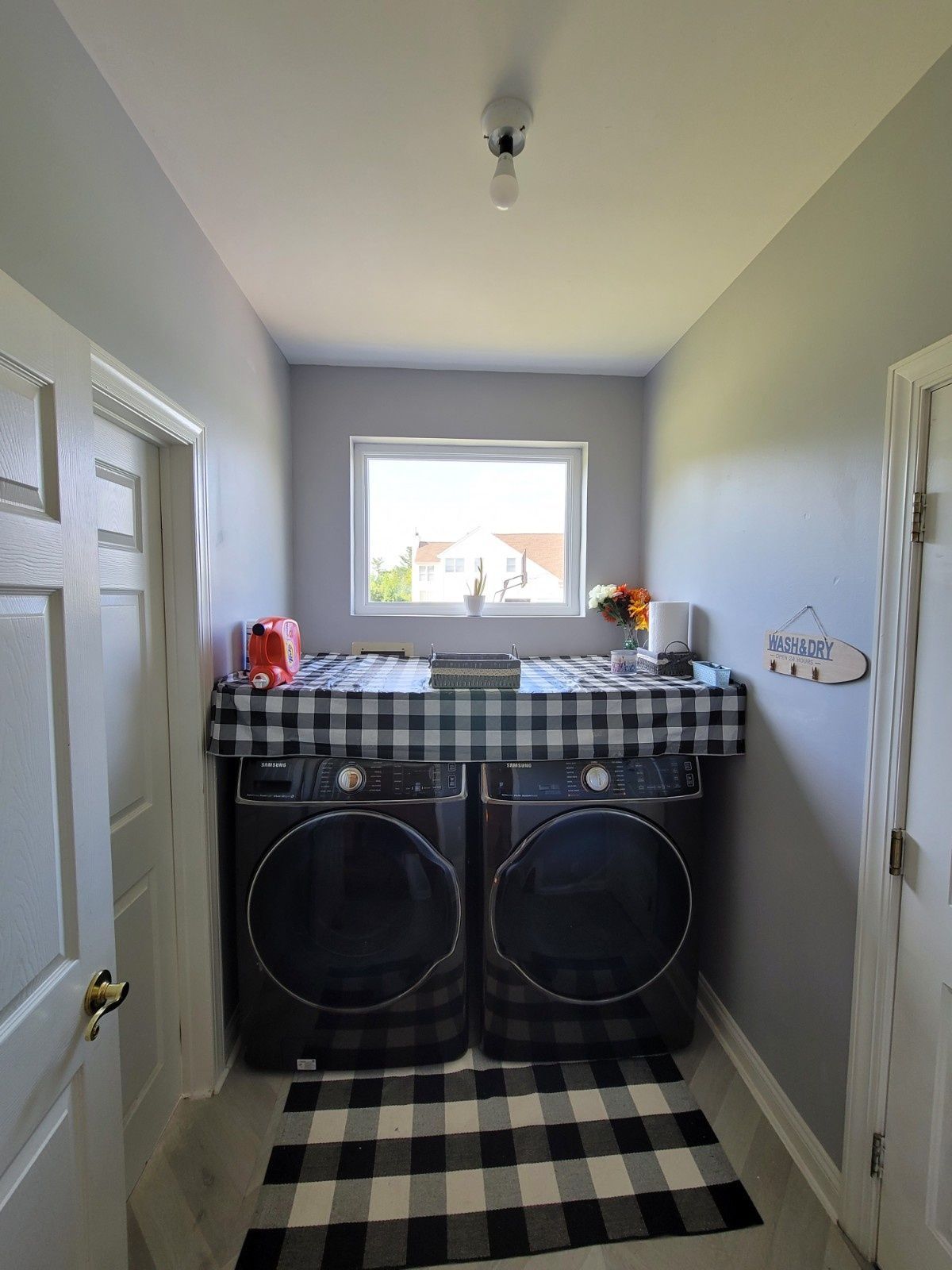A laundry room with two black machines, a buffalo check runner rug, and a matching fabric cover over the laundry units.