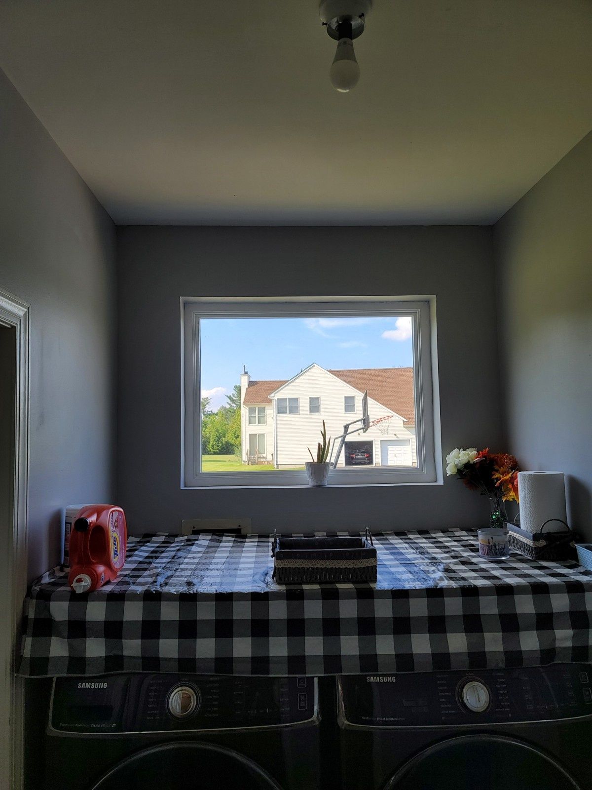 A laundry room with a window overlooking a house, featuring a black-and-white checkered cover over the washing machines.