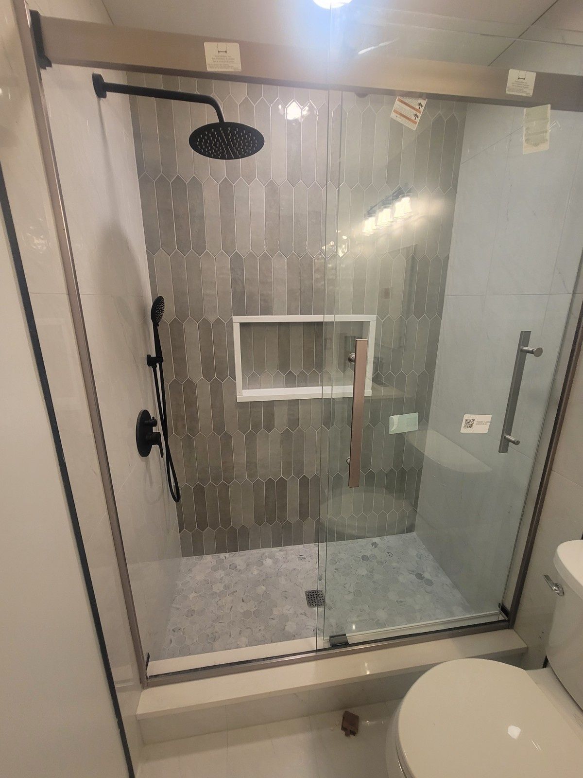 A modern walk-in shower with a glass sliding door, gray patterned tile, a rainfall showerhead, and a built-in niche.