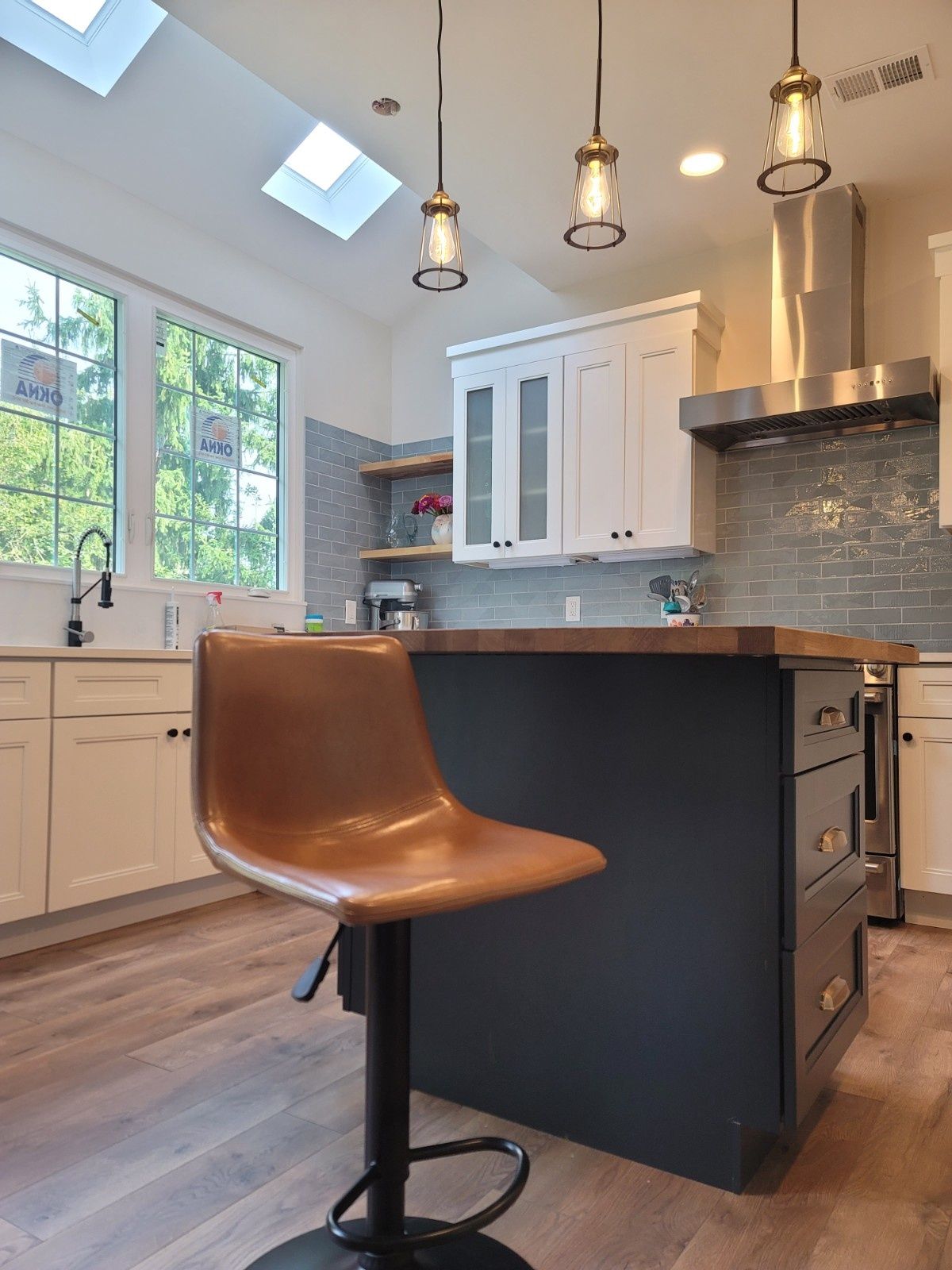 A tan bar stool sits in front of a kitchen island with a dark blue base, white cabinetry, and blue subway tile backsplash.