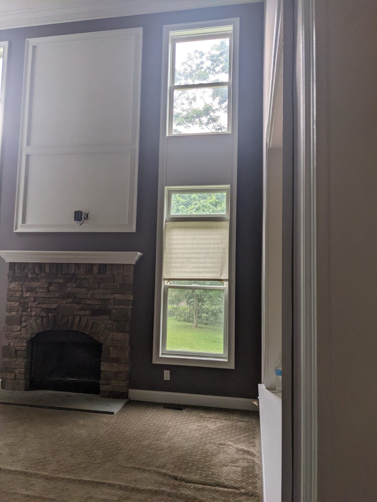 A brick fireplace with a high wall featuring white molding beside tall, stacked windows against a dark purple wall.