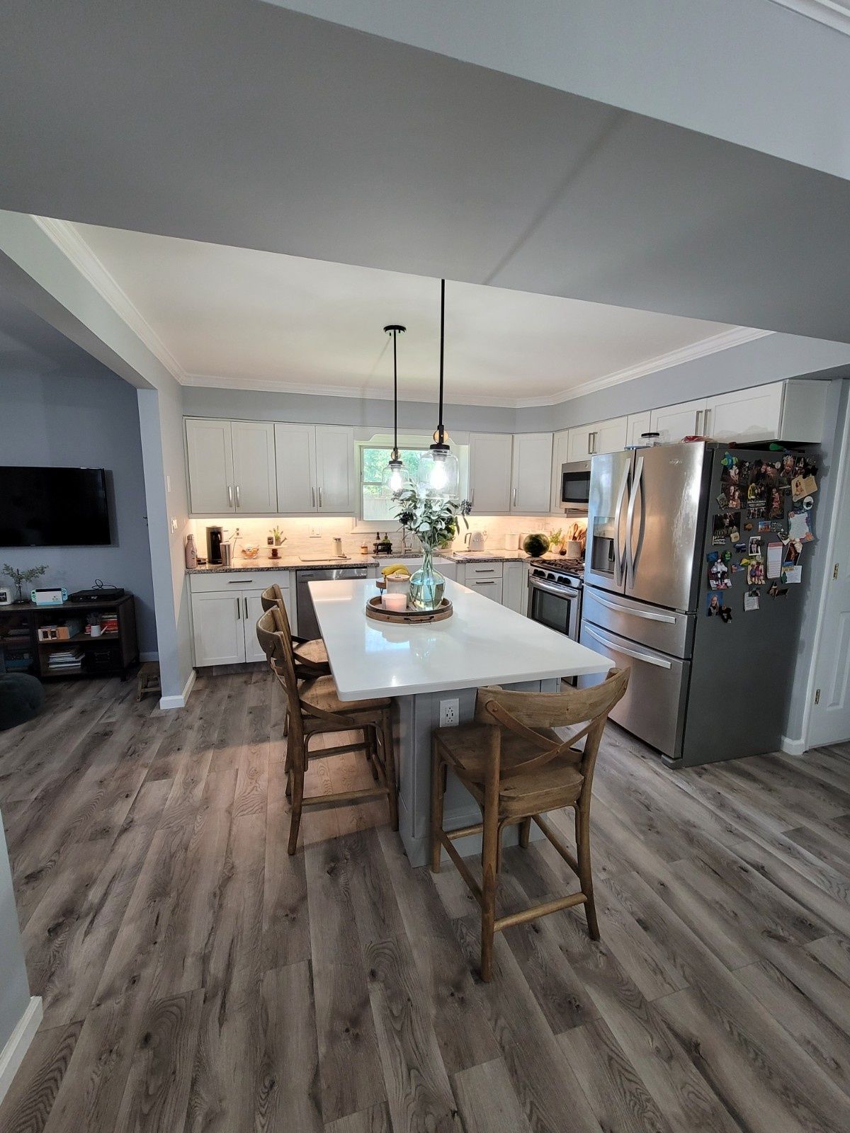 A modern kitchen featuring white cabinets, a large island with two wooden bar stools, and stainless steel appliances.