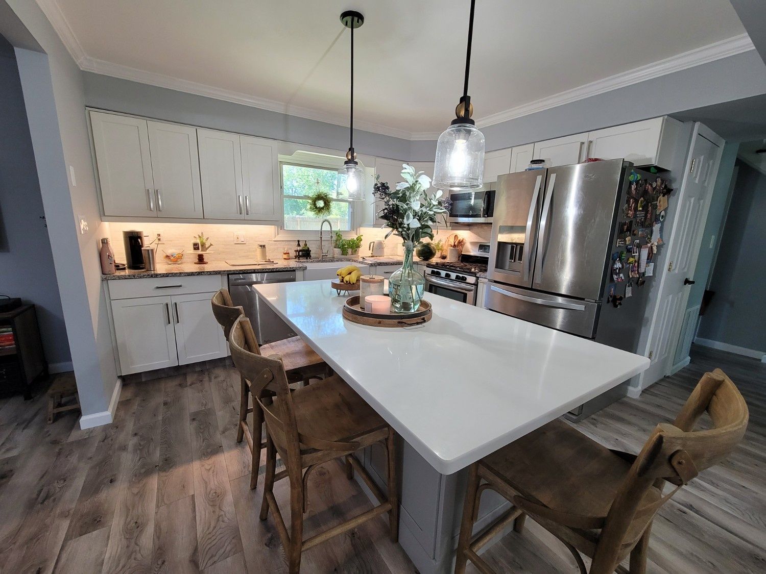 A bright kitchen with white cabinets, a large white island with wooden bar stools, and stainless steel appliances.