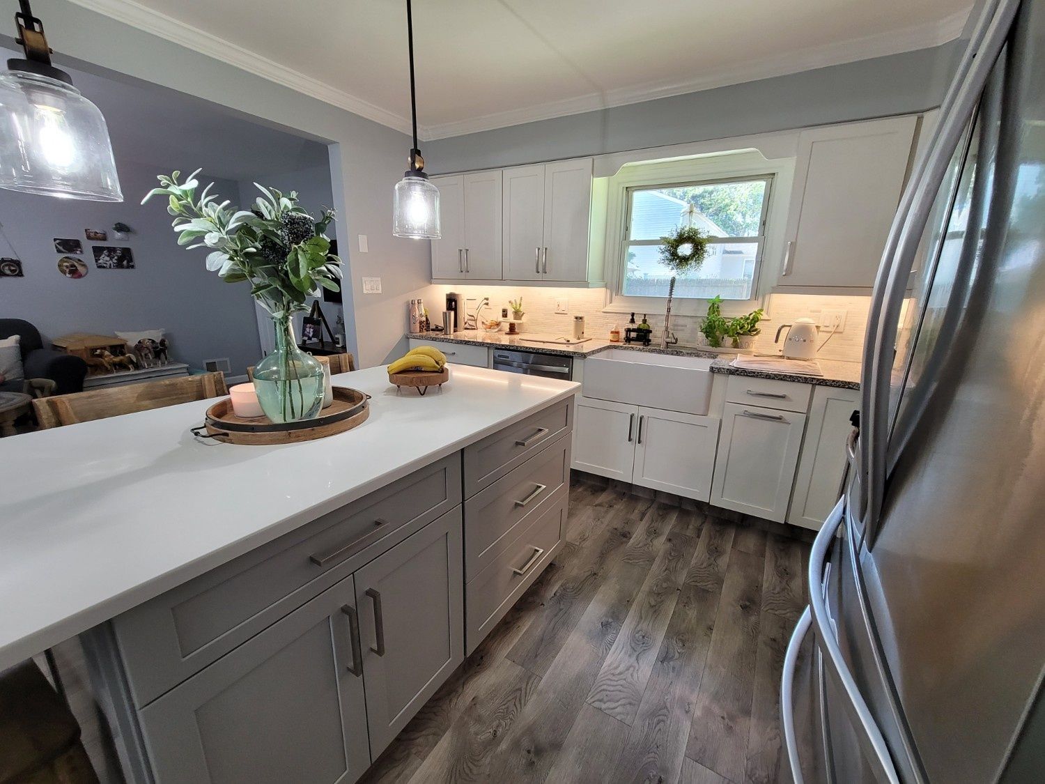 Modern kitchen featuring grey cabinets, white countertops, a central island, and wood-look flooring under pendant lights.