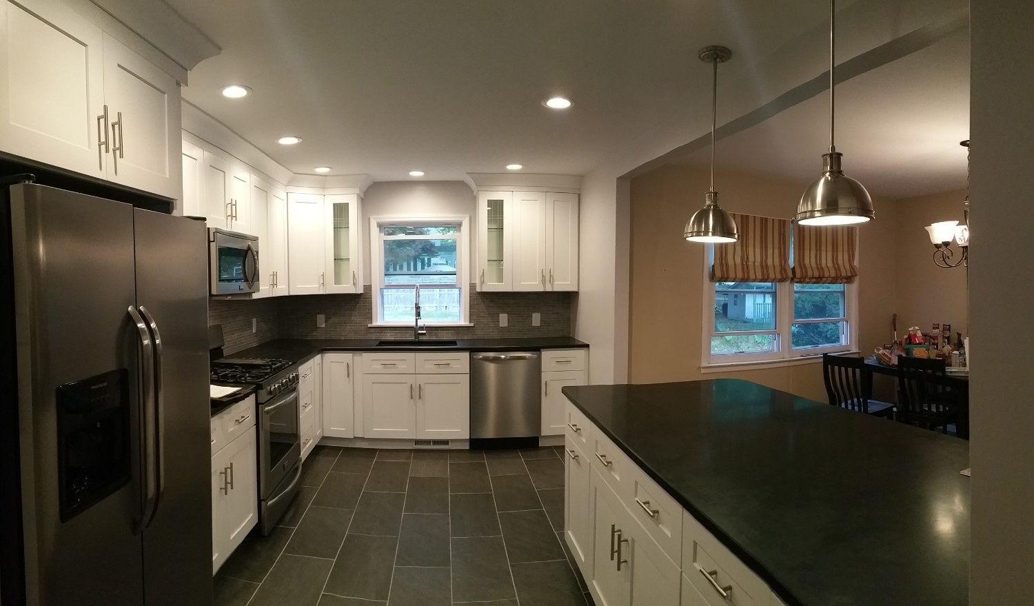 A modern kitchen with white cabinets, dark countertops, stainless steel appliances, and slate flooring.