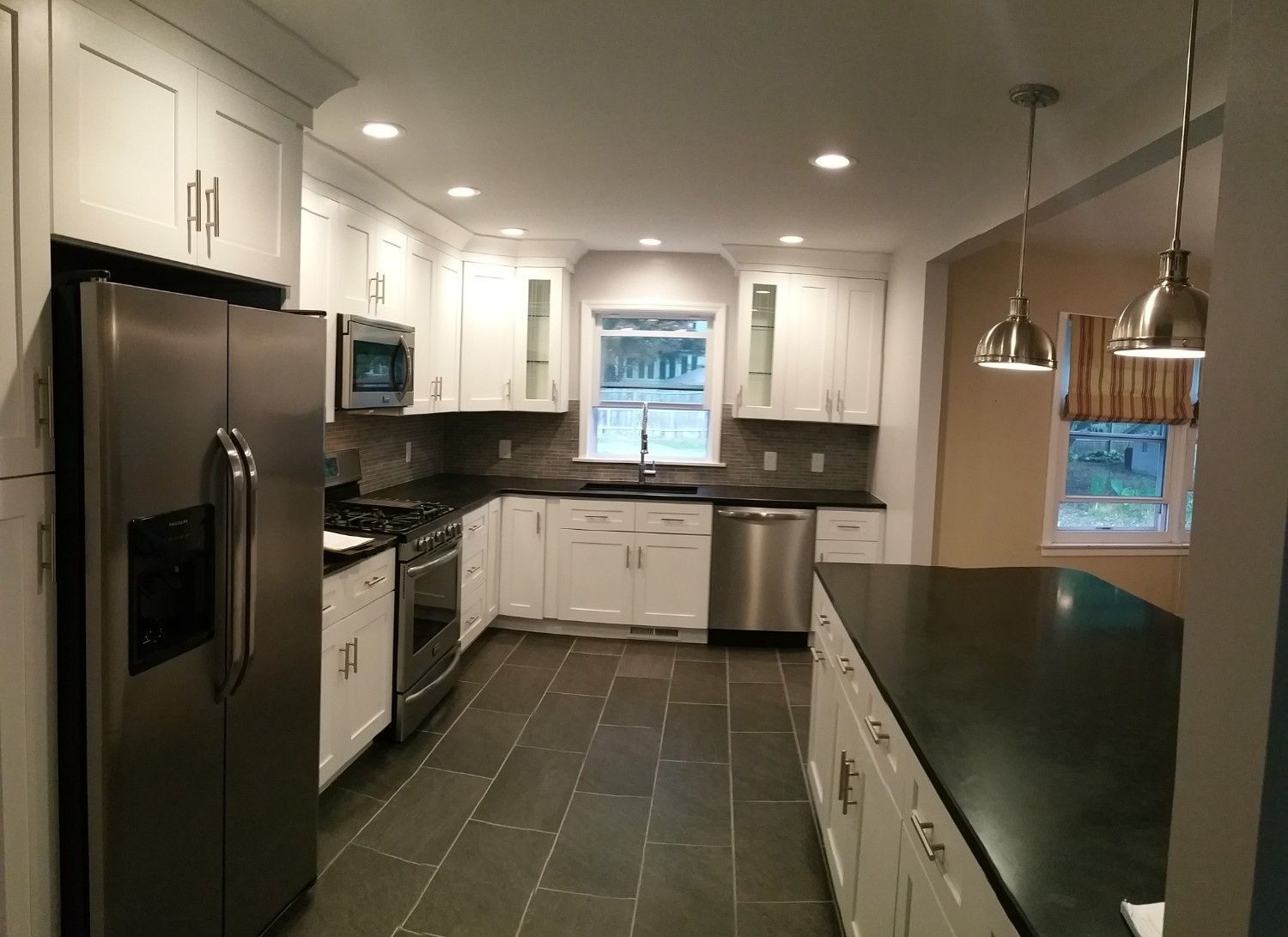 A modern kitchen featuring white cabinets, stainless steel appliances, a dark countertop, and slate tile floors.
