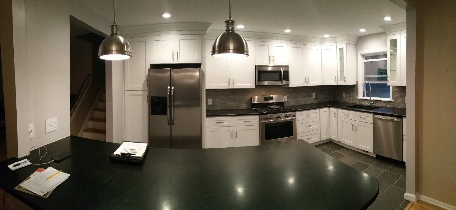 A wide-angle shot of a modern kitchen with white cabinets, dark countertops, and stainless steel appliances.