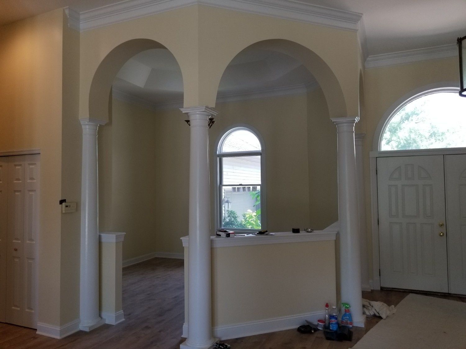 An interior view of a room with yellow walls, white trim, arched openings supported by white columns, and a large window.