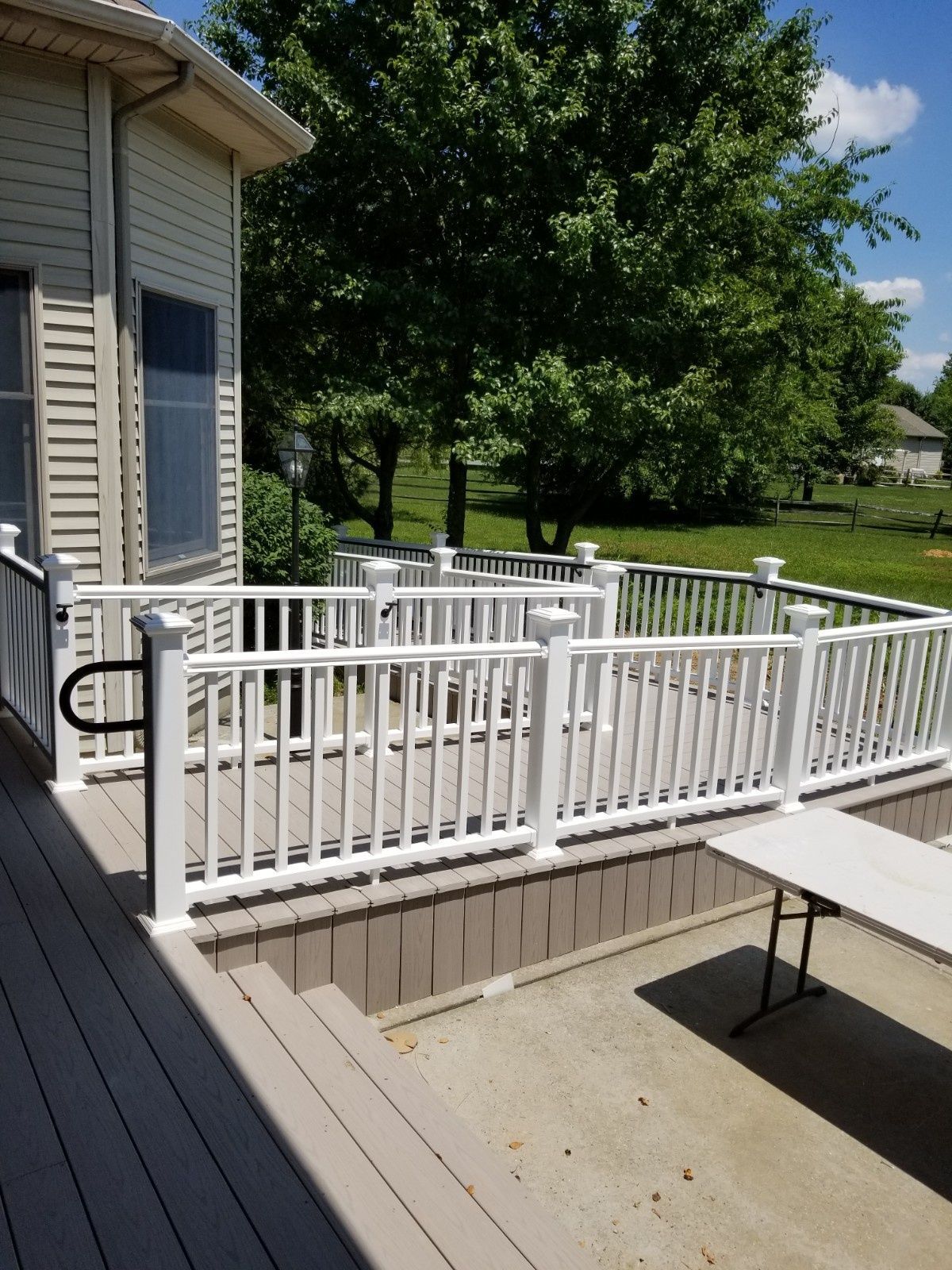 A wooden deck featuring a white railing ramp for wheelchair access, extending from the side of a house onto a patio.