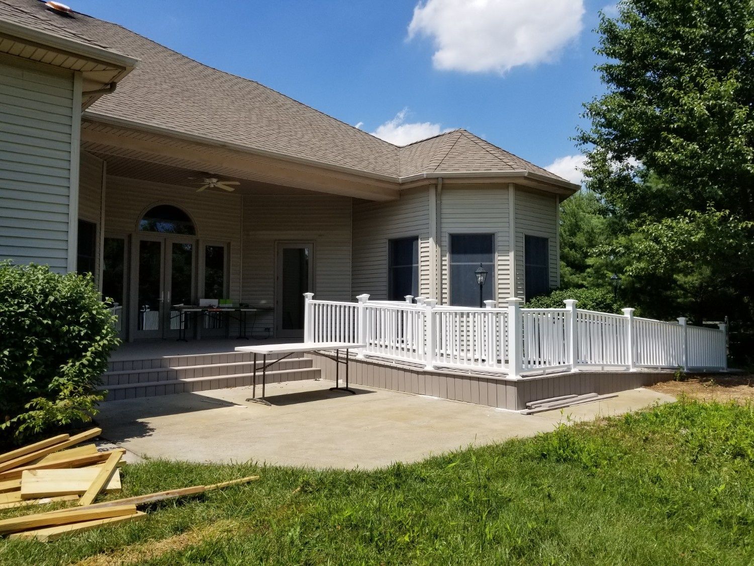 A tan-sided house features a wide, white-railed deck with an accessible ramp leading to a concrete patio.