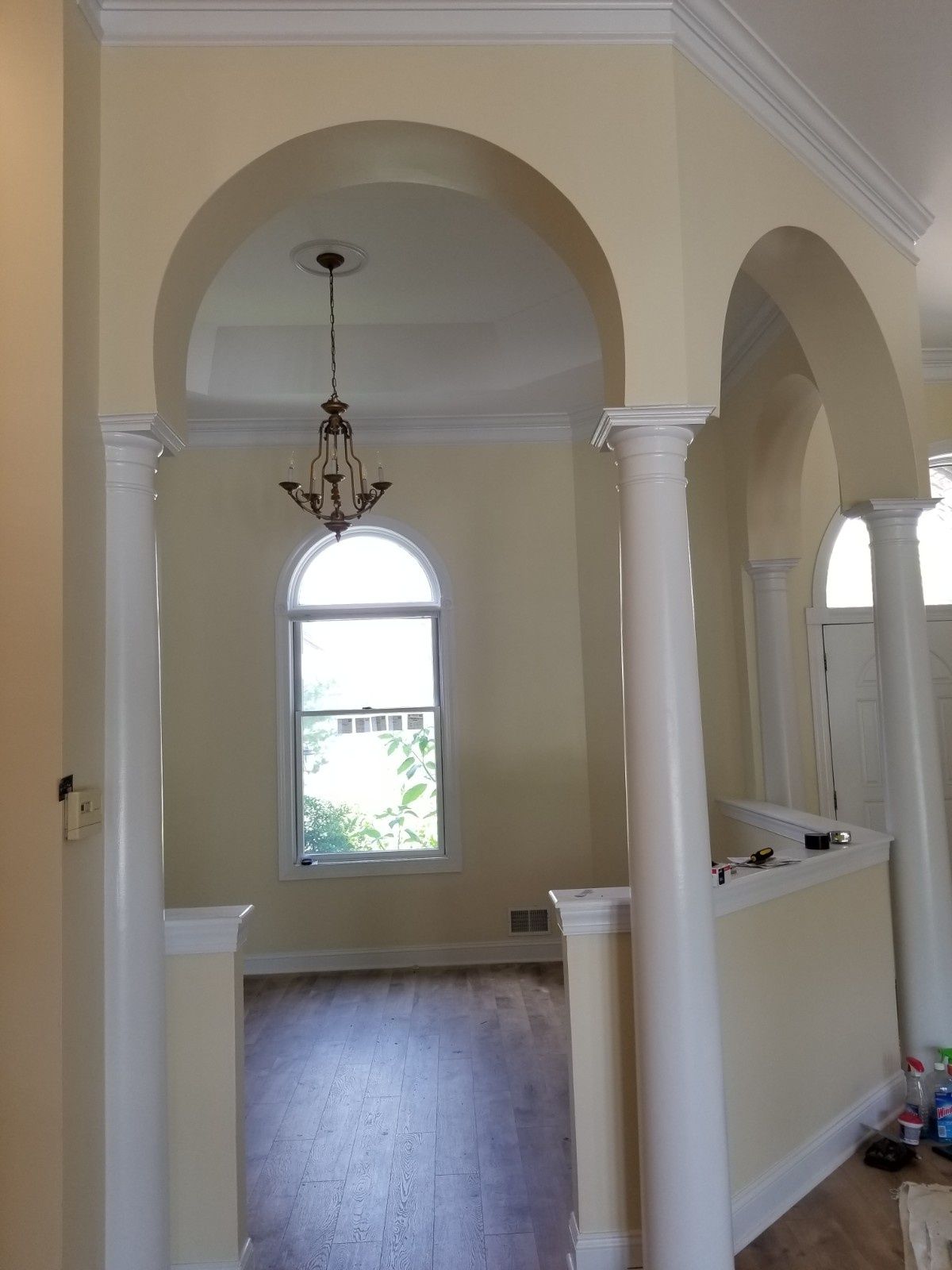 A brightly lit room entryway featuring two white columns supporting arched doorways, leading to a window and chandelier.