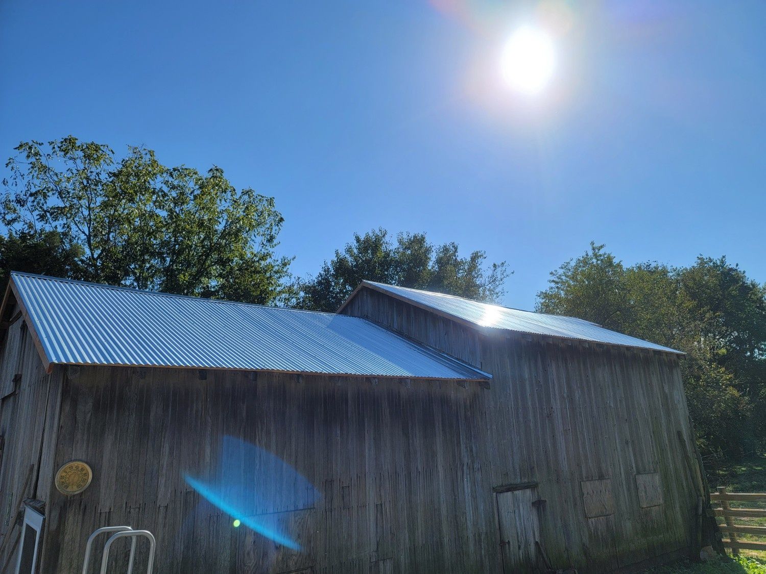 A weathered wooden barn with a shiny, new corrugated metal roof under a bright, sunny blue sky.