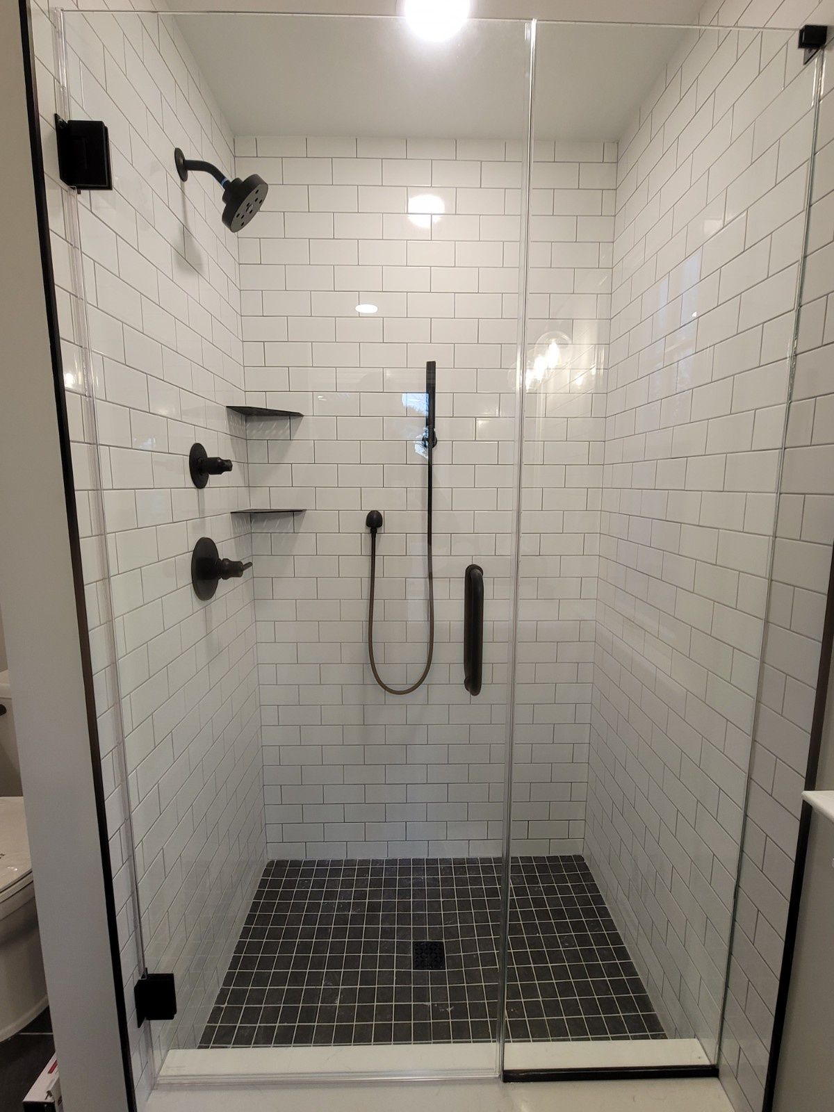 A walk-in shower with white subway tile walls, a dark grey tiled floor, matte black fixtures, and a glass door.