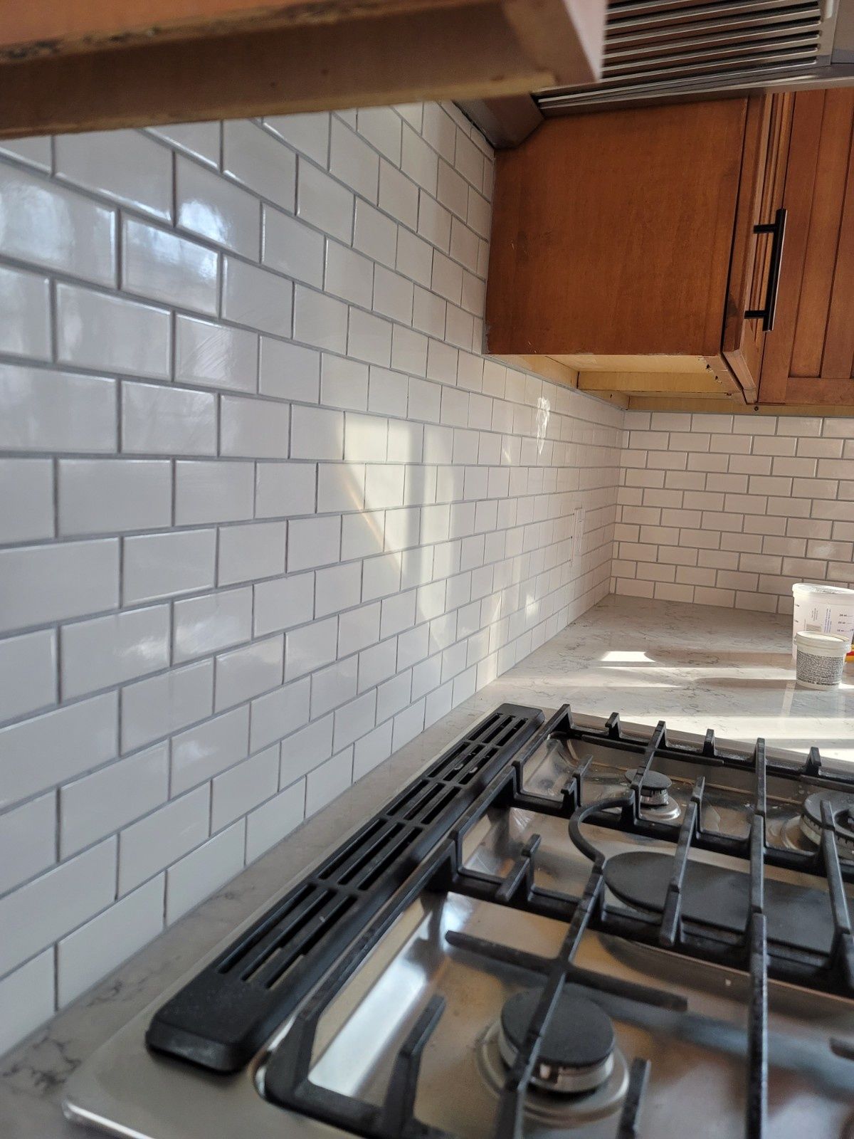 A close-up of a kitchen backsplash with white subway tiles installed behind a stainless steel gas stovetop.