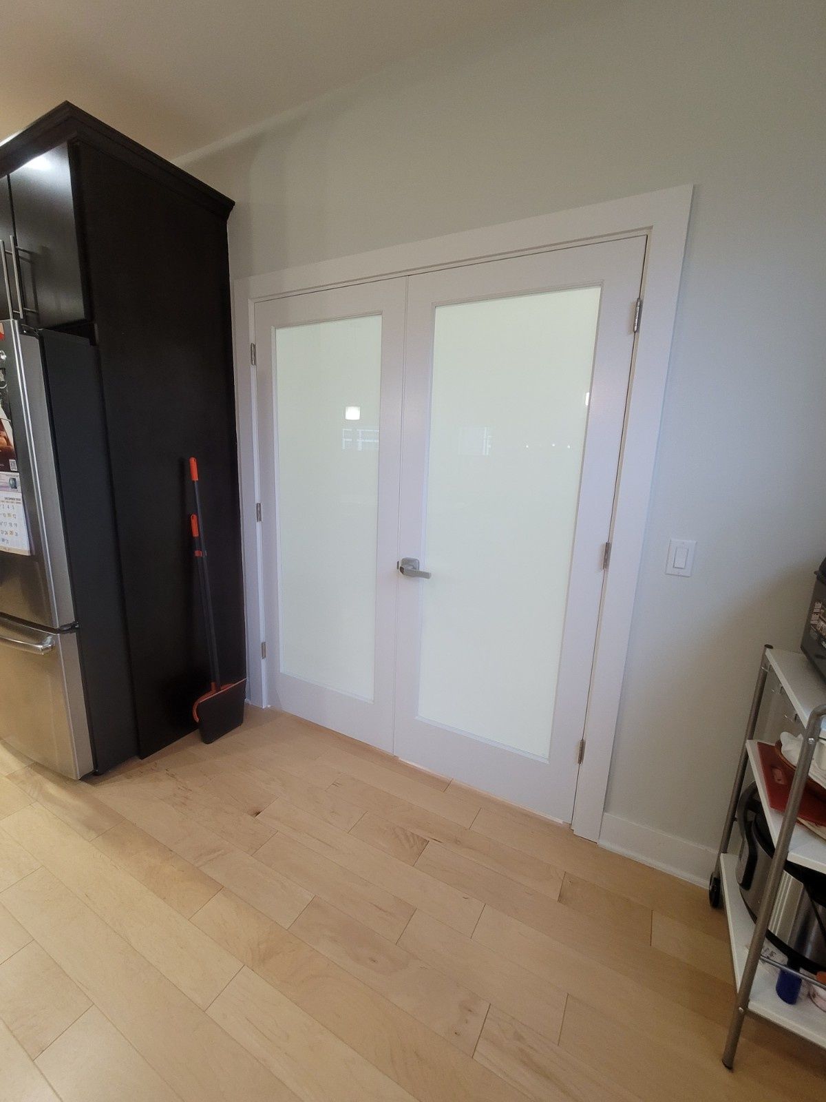 White French doors with frosted glass in a room with light wood floors and a black cabinet to the left.