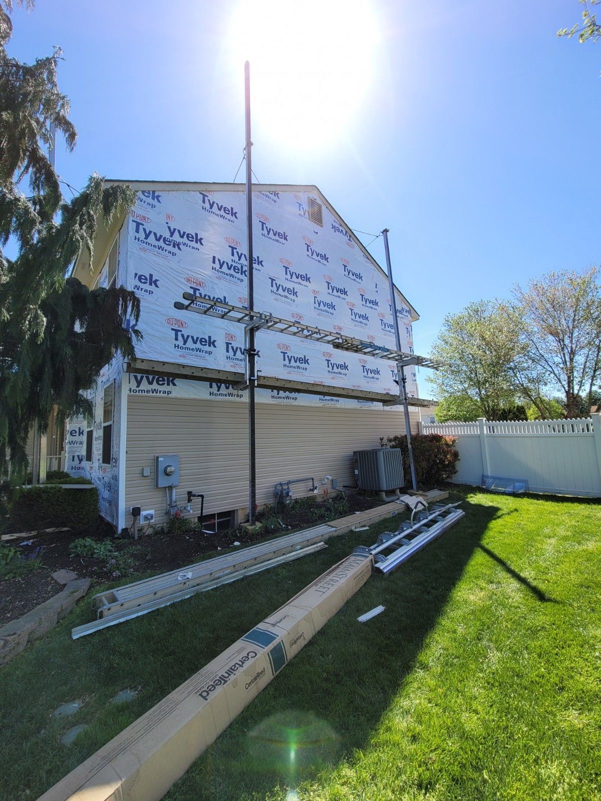 A residential home under renovation with Tyvek house wrap on the upper level and vinyl siding on the lower level.
