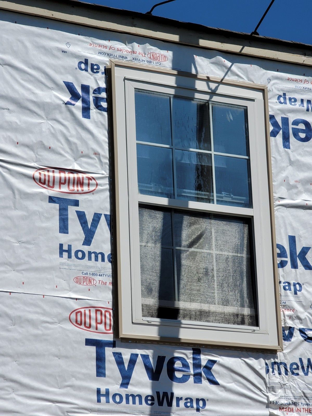 A single-hung window with a white frame installed in a wall covered by white Tyvek house wrap.
