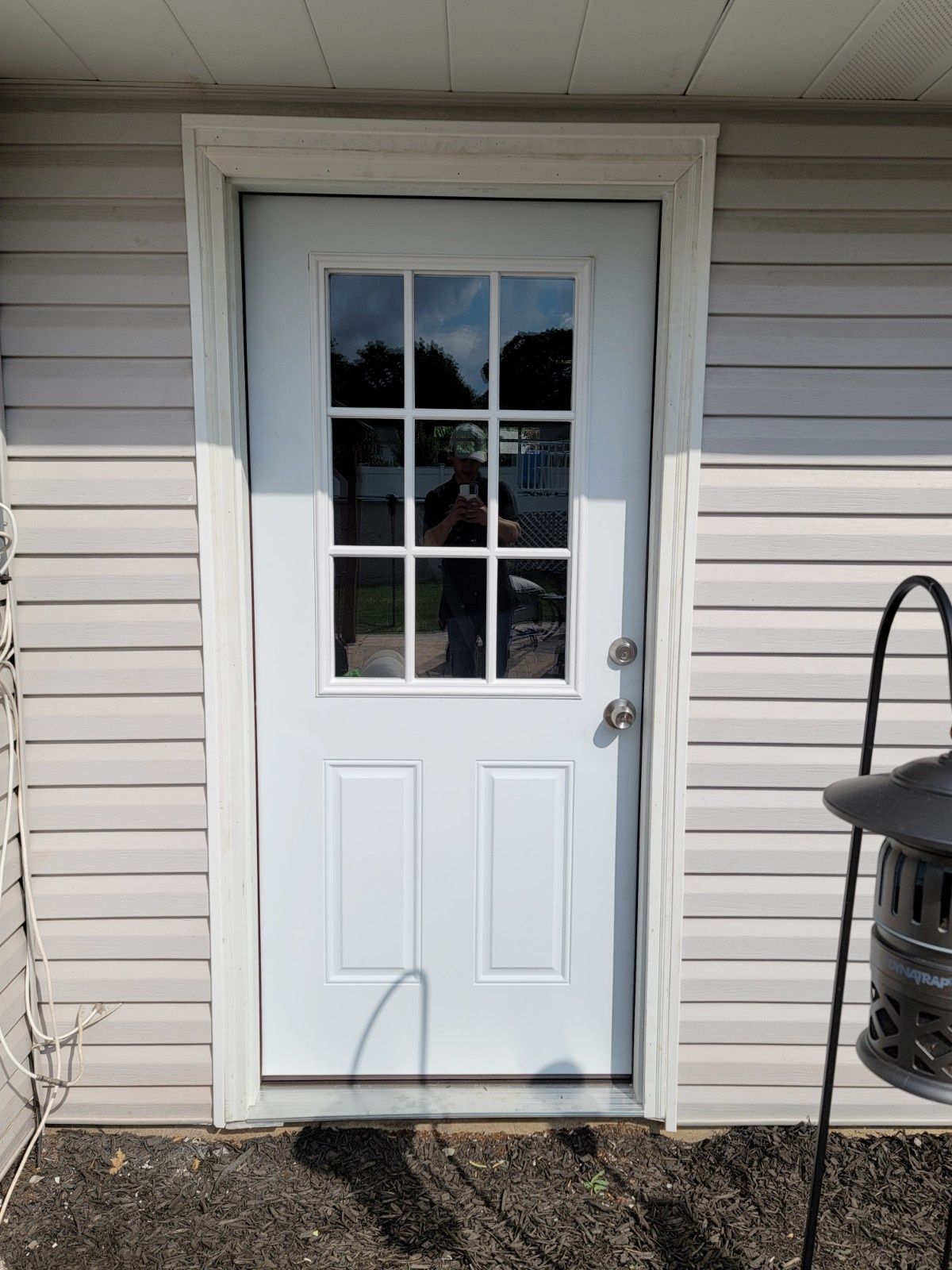A white entry door with a nine-pane window at the top, installed in a home with light-colored horizontal siding.