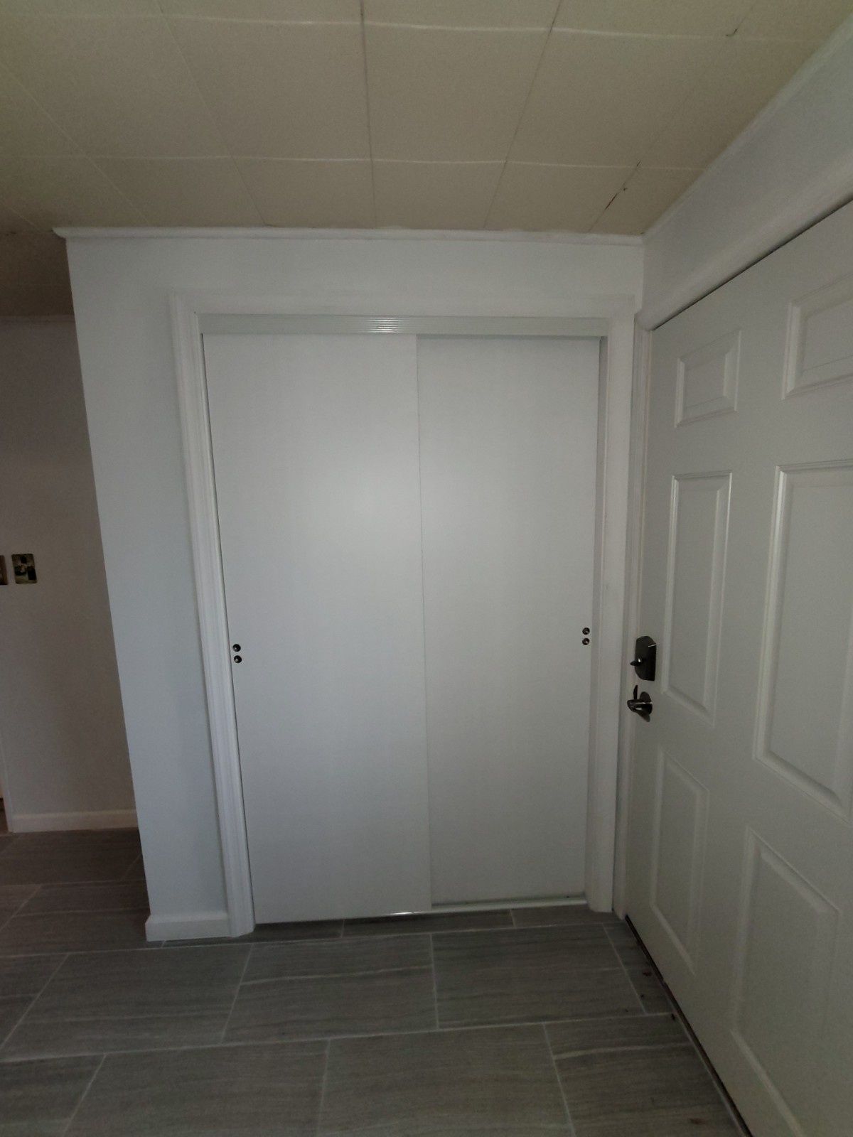 A white sliding closet door next to a white entry door in a room with gray tiled flooring.