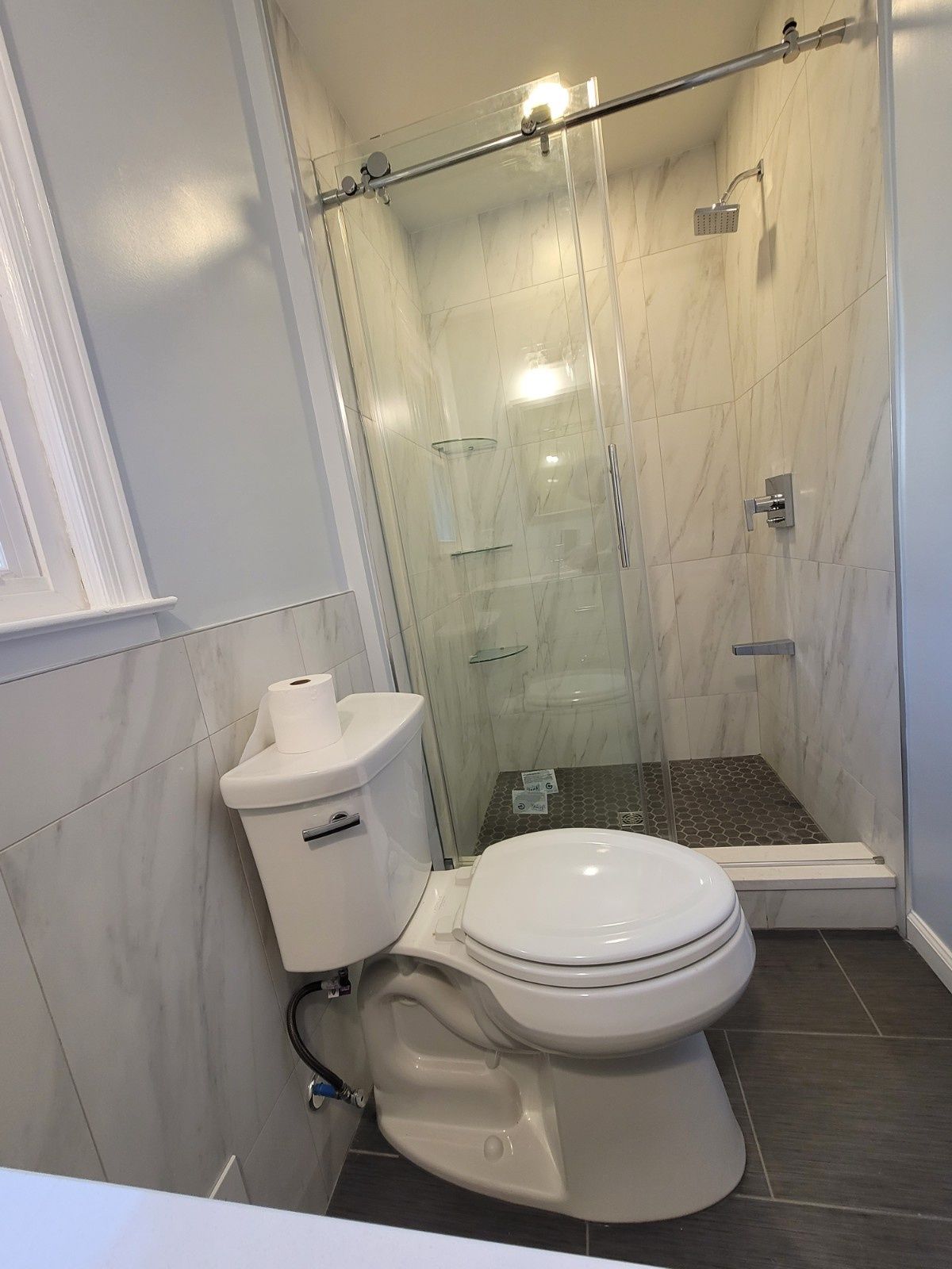 A modern bathroom featuring a white toilet in the foreground and a glass-enclosed shower with tiled walls in the back.