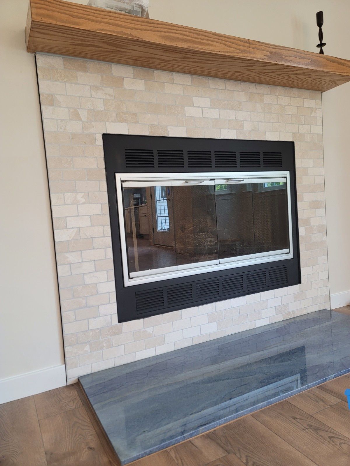 Fireplace with a stone tile surround, wooden mantel, and dark gray slab hearth in a living room.
