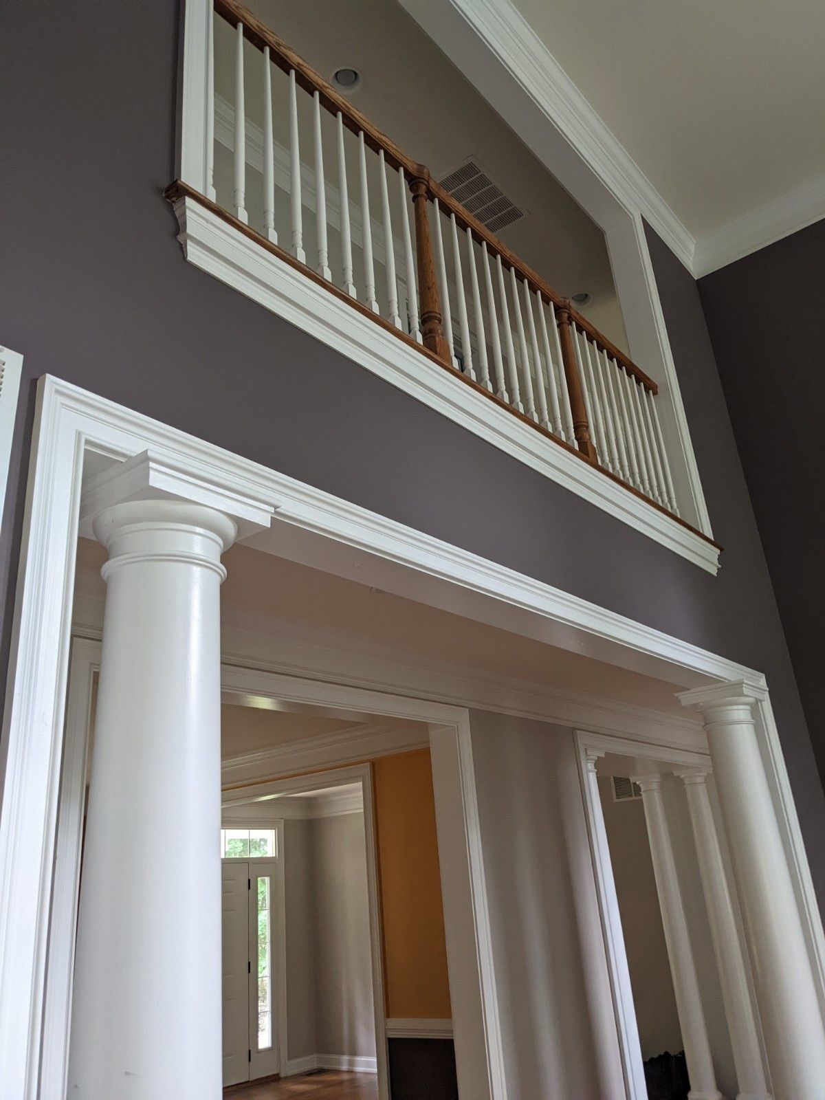 A view looking up at a dark gray wall with an interior white railing balcony above a decorative white arched doorway.