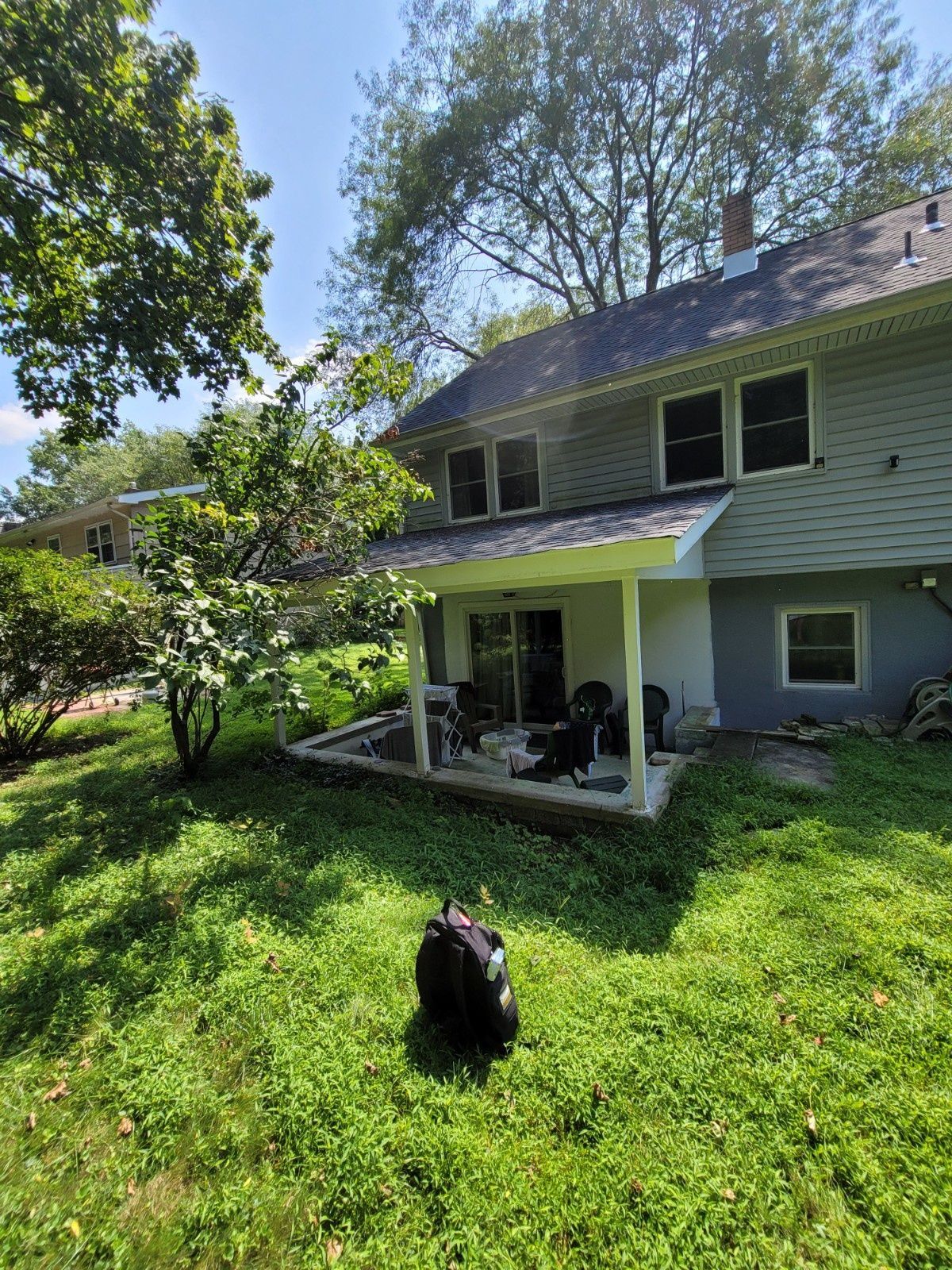 A gray house with a small covered patio and a grassy yard, with a dark backpack sitting in the foreground.