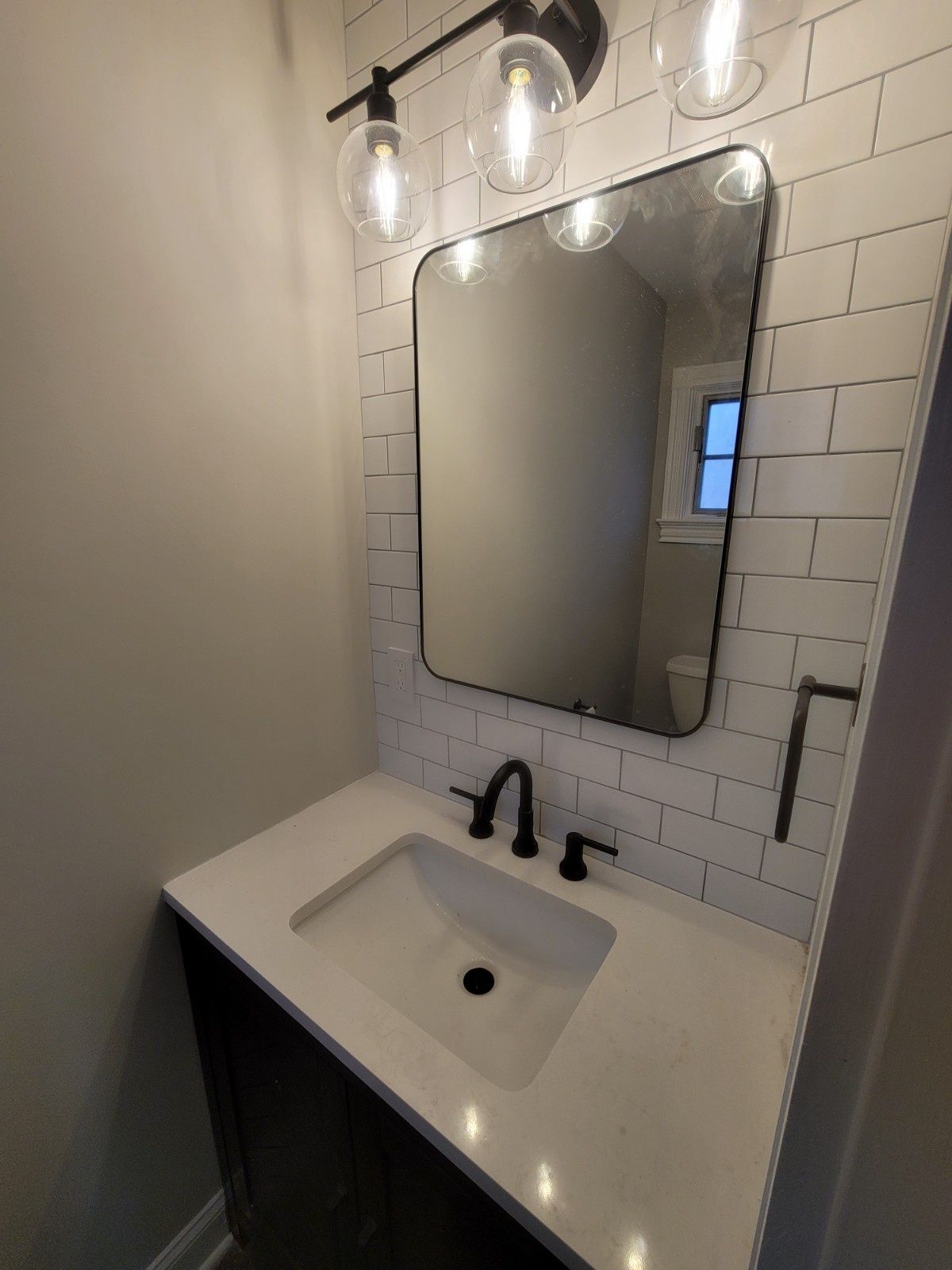 A bathroom vanity with a white countertop, black sink faucet, rectangular mirror, and white subway tile backsplash.