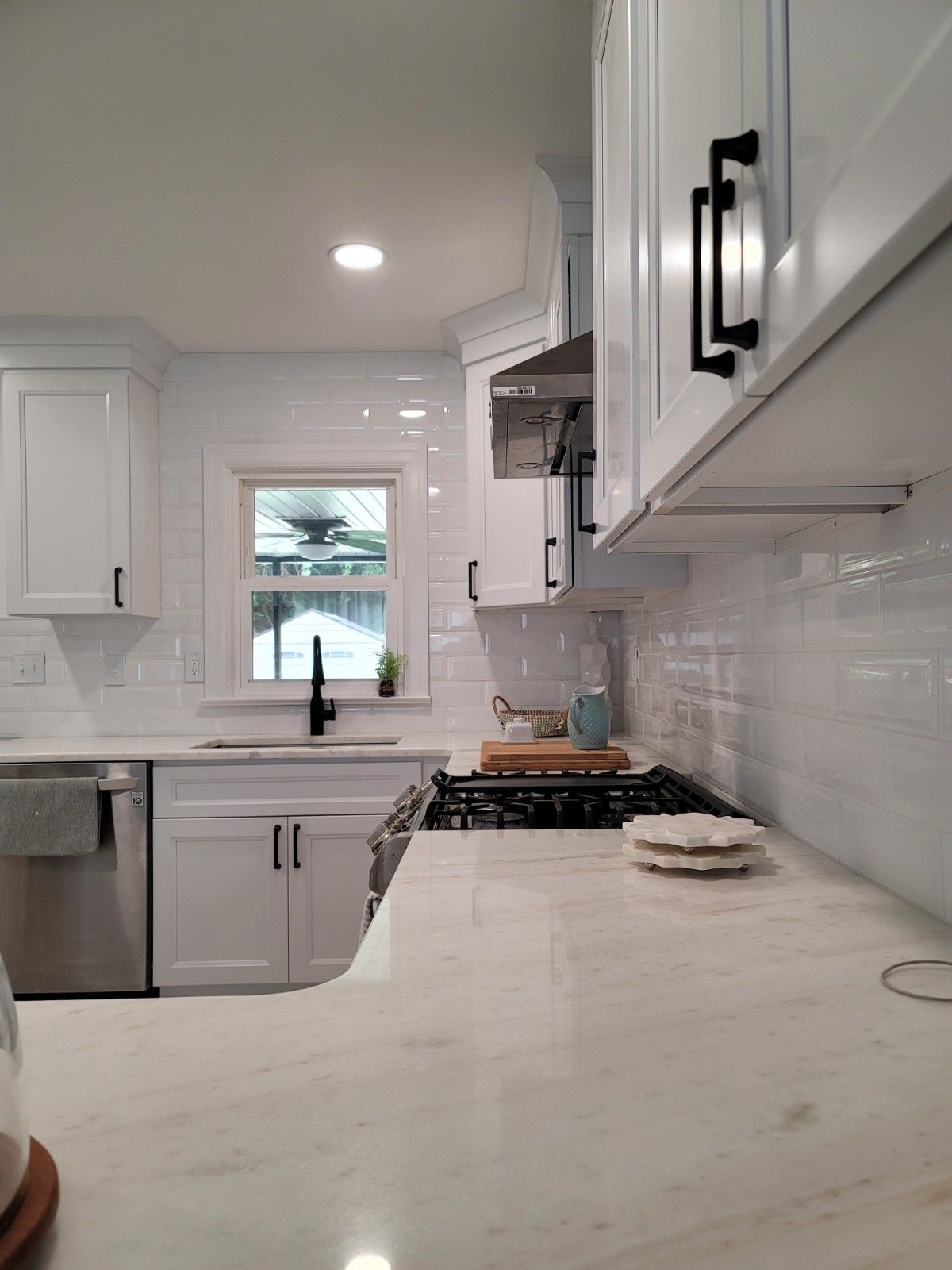 White kitchen with marble countertops, shaker cabinets, subway tile backsplash, and black hardware.