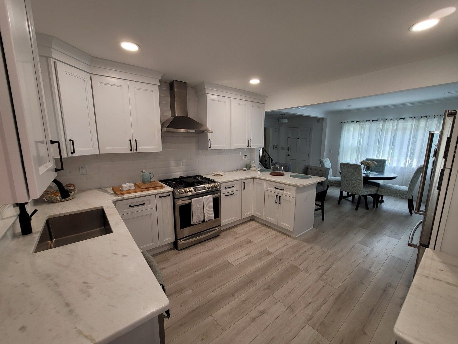 A modern kitchen with white cabinets, stainless steel appliances, and marble-look countertops, leading into a dining area.