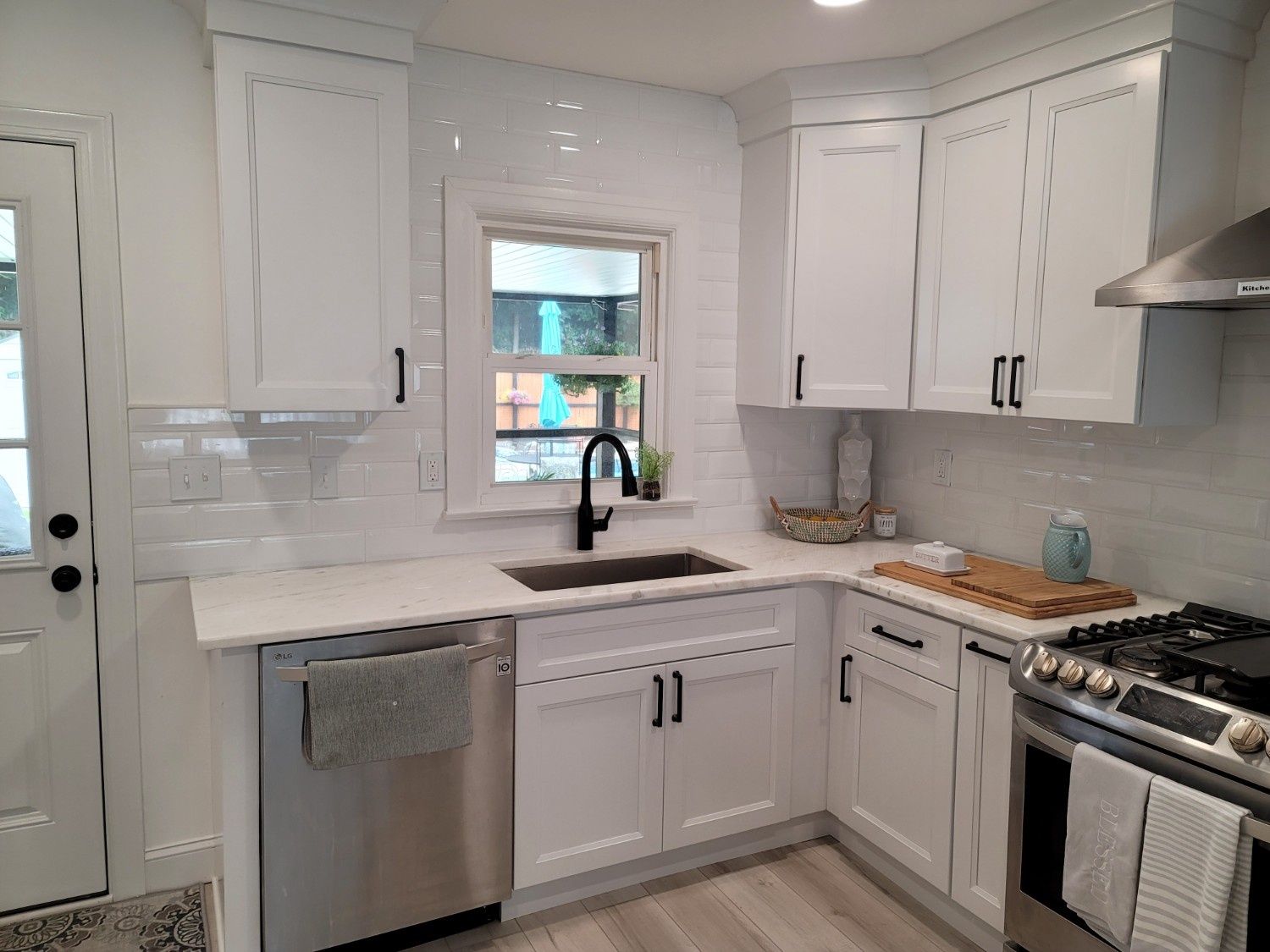 A bright modern kitchen with white cabinets, a farmhouse sink, stainless steel appliances, and a light-colored countertop.