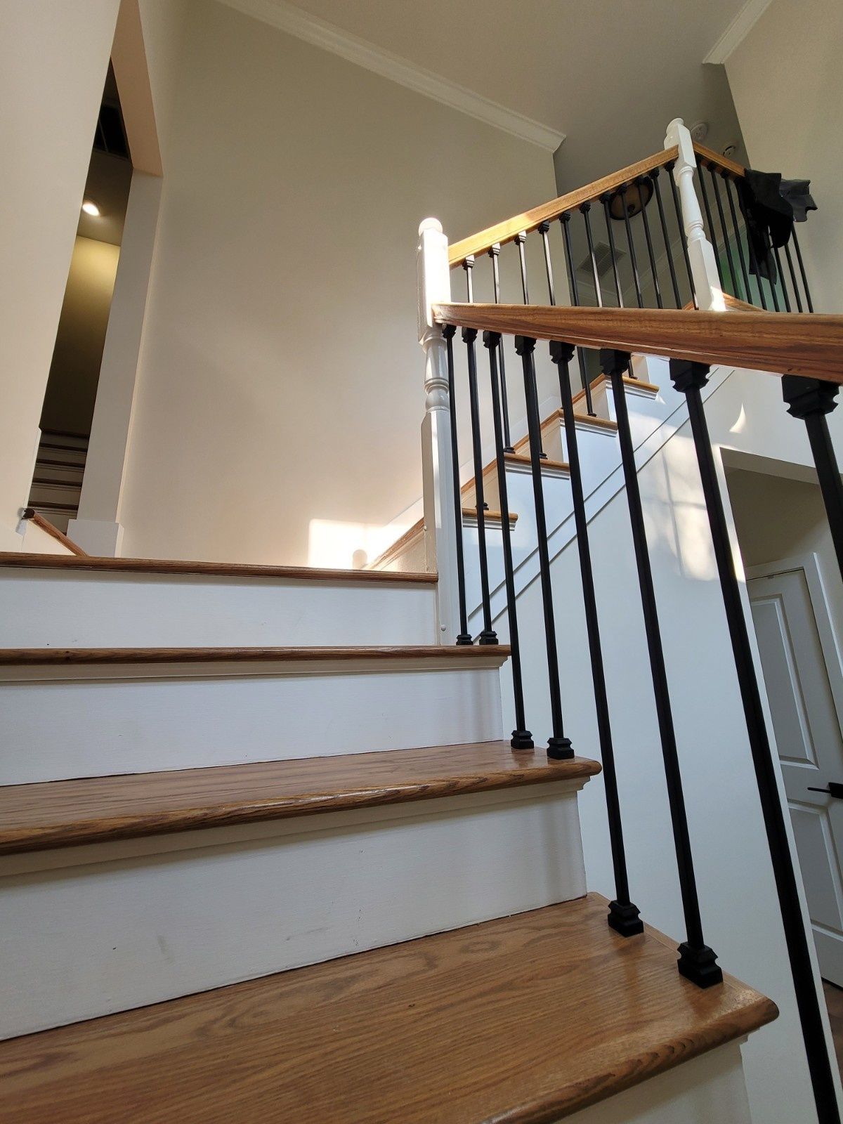 A staircase with wooden steps, white risers, and a railing with white posts and thin black metal balusters.
