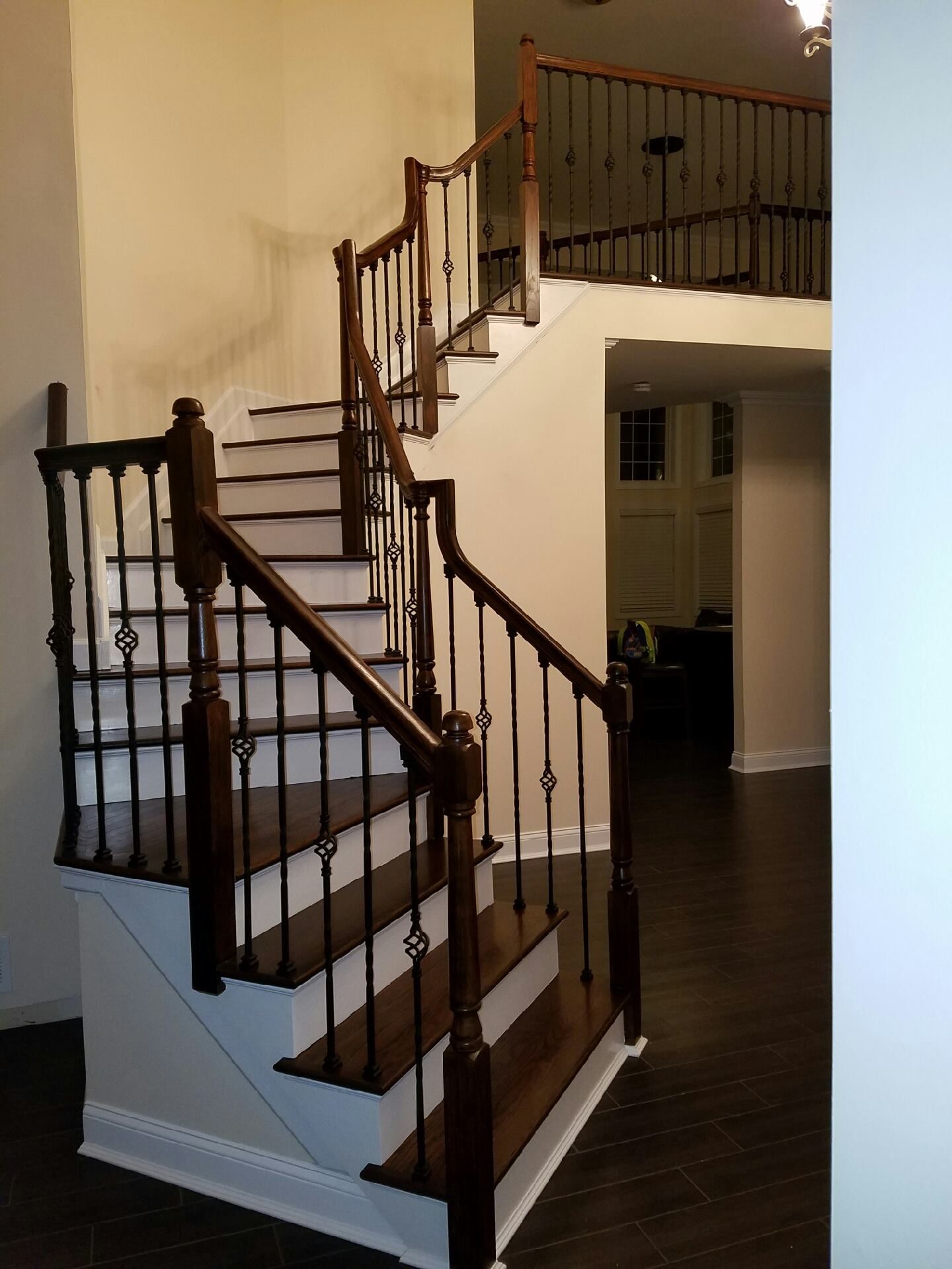 A wooden staircase with dark steps and railings, featuring a landing and a second-floor walkway, in a bright home interior.