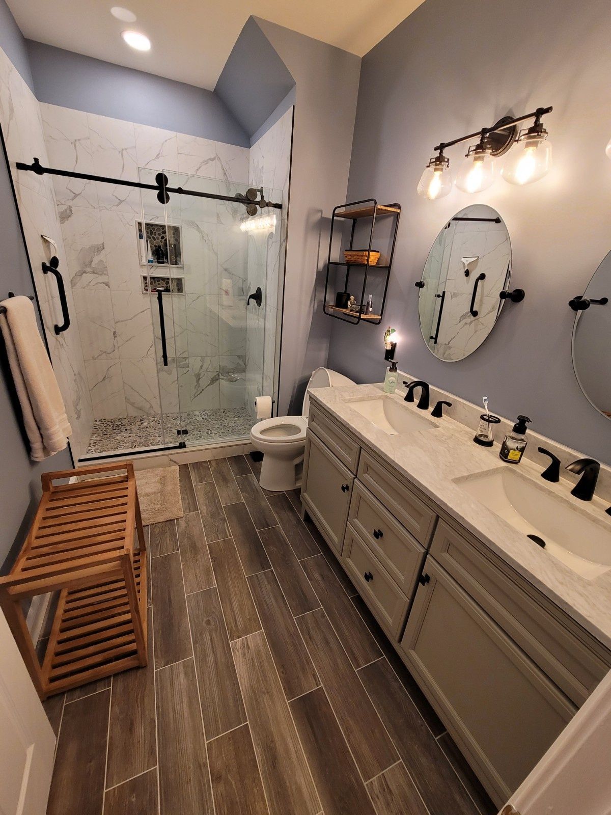 Modern bathroom featuring a wood-look tile floor, double vanity with gray cabinets, walk-in glass shower, and blue walls.