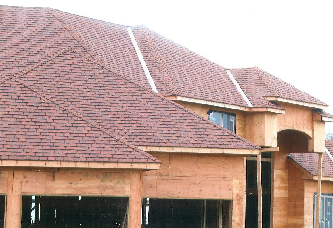 A partially constructed house frame with a completed red shingled roof, seen on an overcast day.