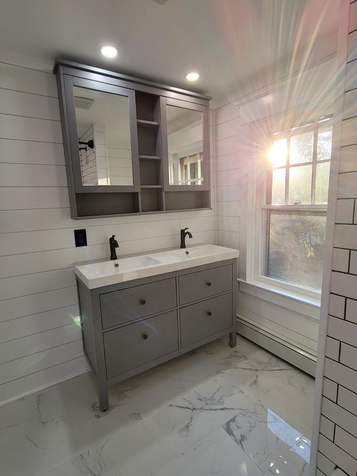 A bathroom vanity with a gray cabinet and double sinks, featuring a mirrored medicine cabinet and white shiplap walls.