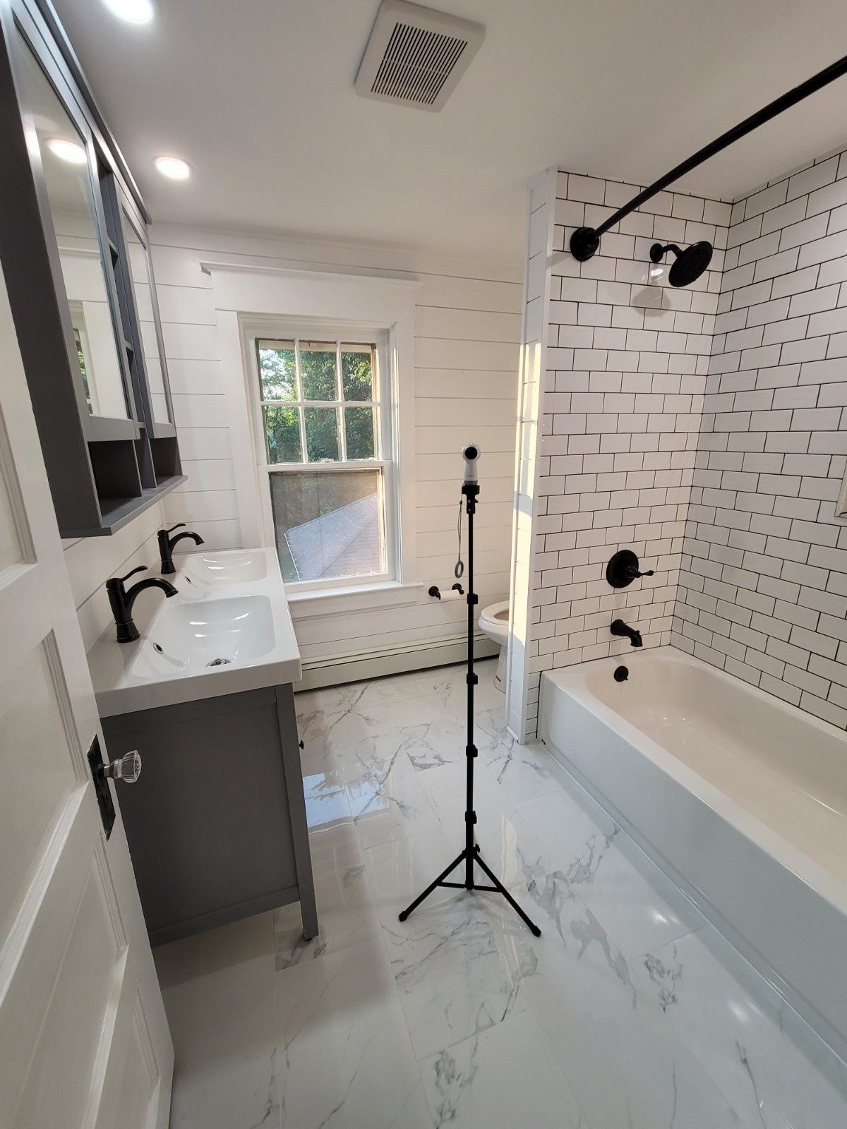 A modern bathroom with a double vanity, a white subway tile bathtub, and marble-look flooring.