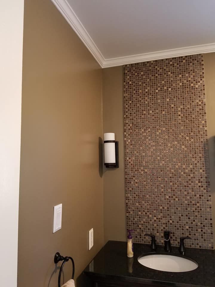 A bathroom vanity featuring a sink, dark countertop, a mosaic tile backsplash, and a wall-mounted light fixture.