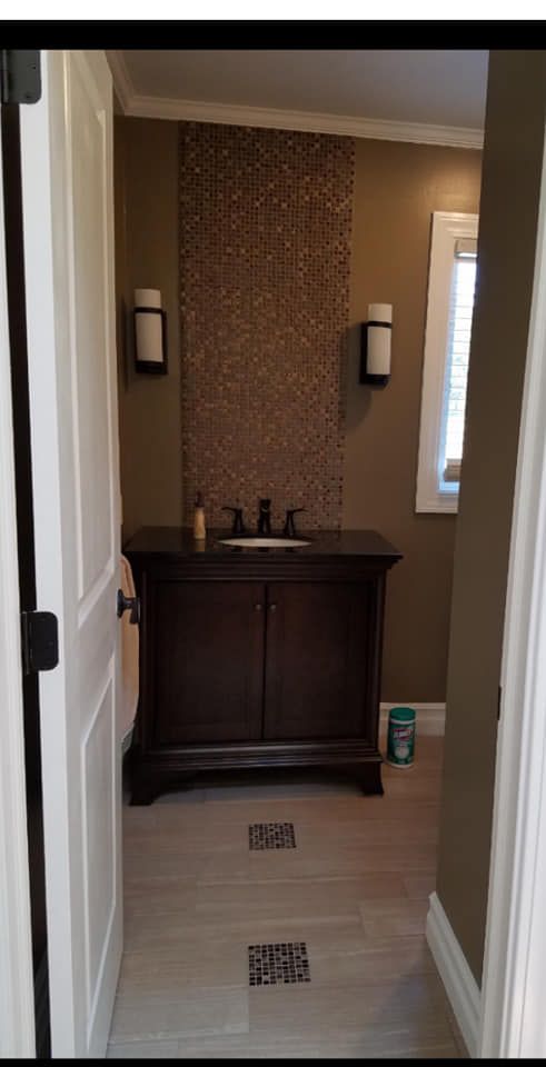A bathroom vanity with a dark wood cabinet, vessel sink, and a vertical feature wall of patterned tile between two lamps.