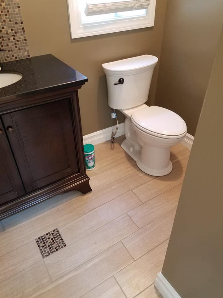 A bathroom with wood-look tile flooring, a dark wood vanity with a stone countertop, and a white toilet by a window.