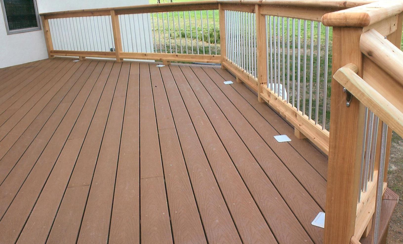 A brown composite deck with a wooden railing and vertical metal balusters, viewed from a slightly elevated angle.