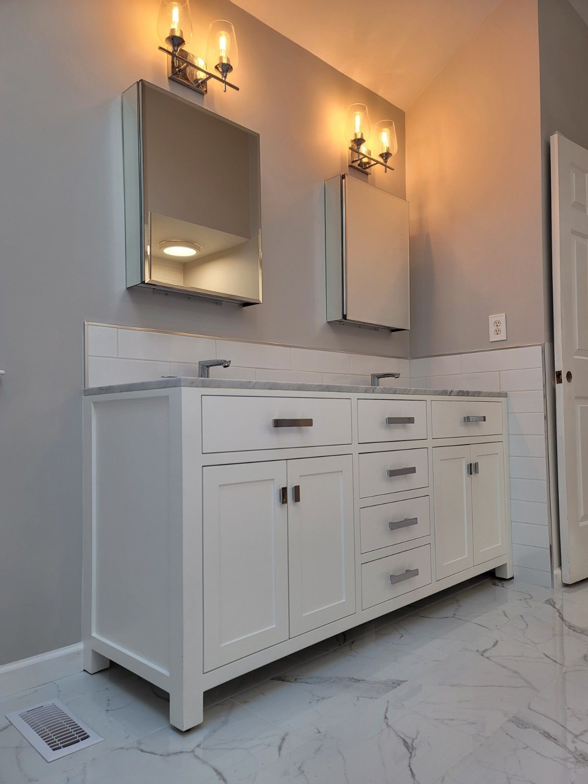 A modern bathroom vanity with two white cabinets, marble-patterned flooring, and two wall-mounted medicine cabinets.